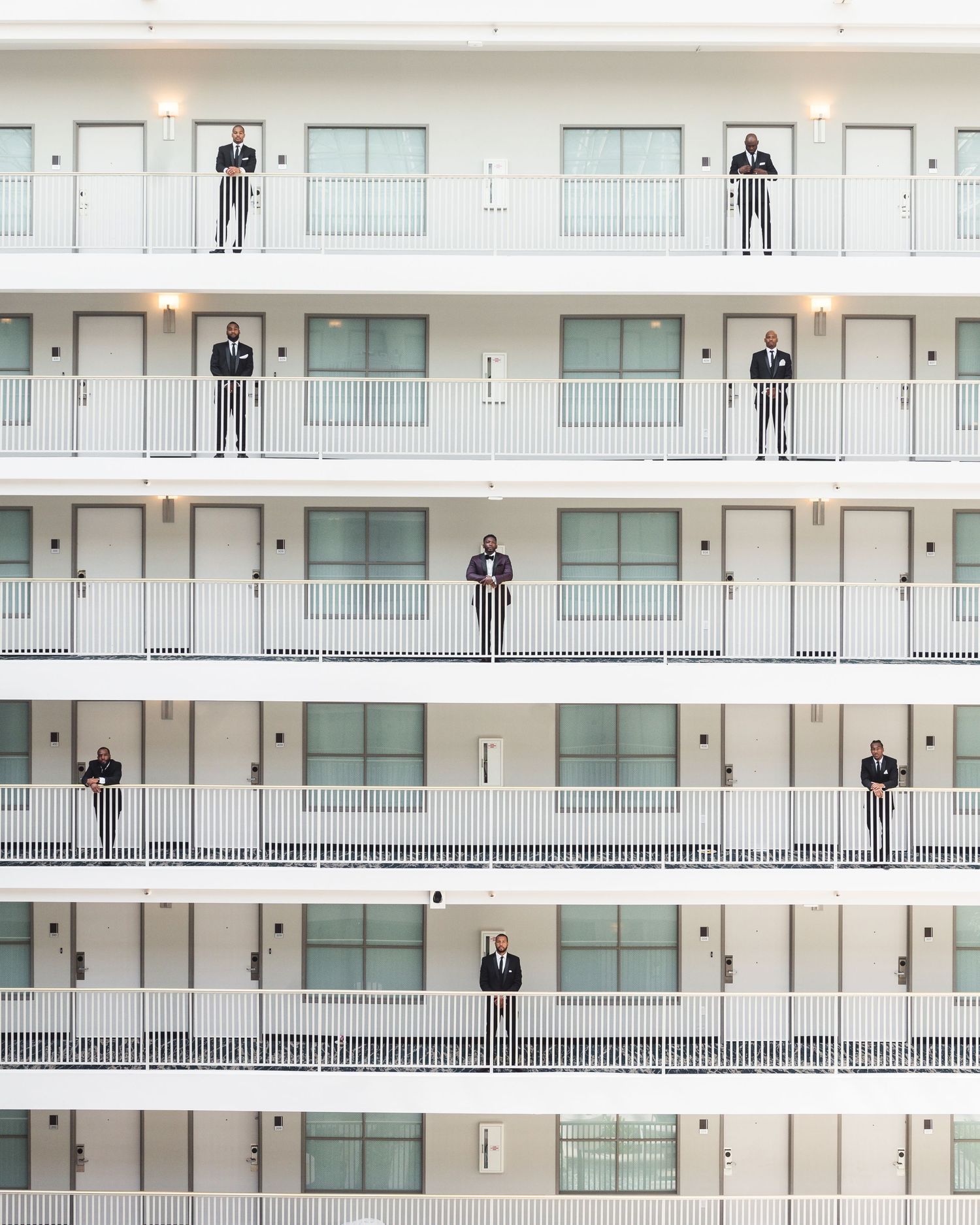 Figures stand on identical white apartment balconies in a symmetrical architectural composition.
