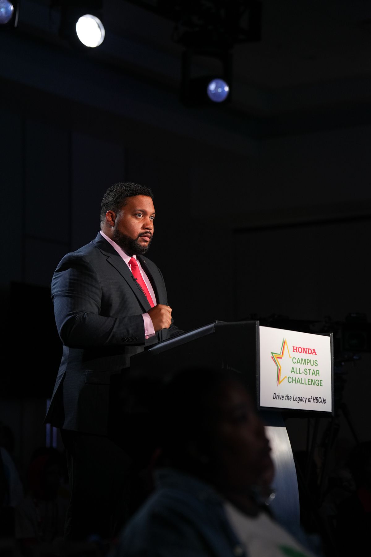 Man in suit speaking at Honda Campus All-Star Challenge podium during academic competition event.