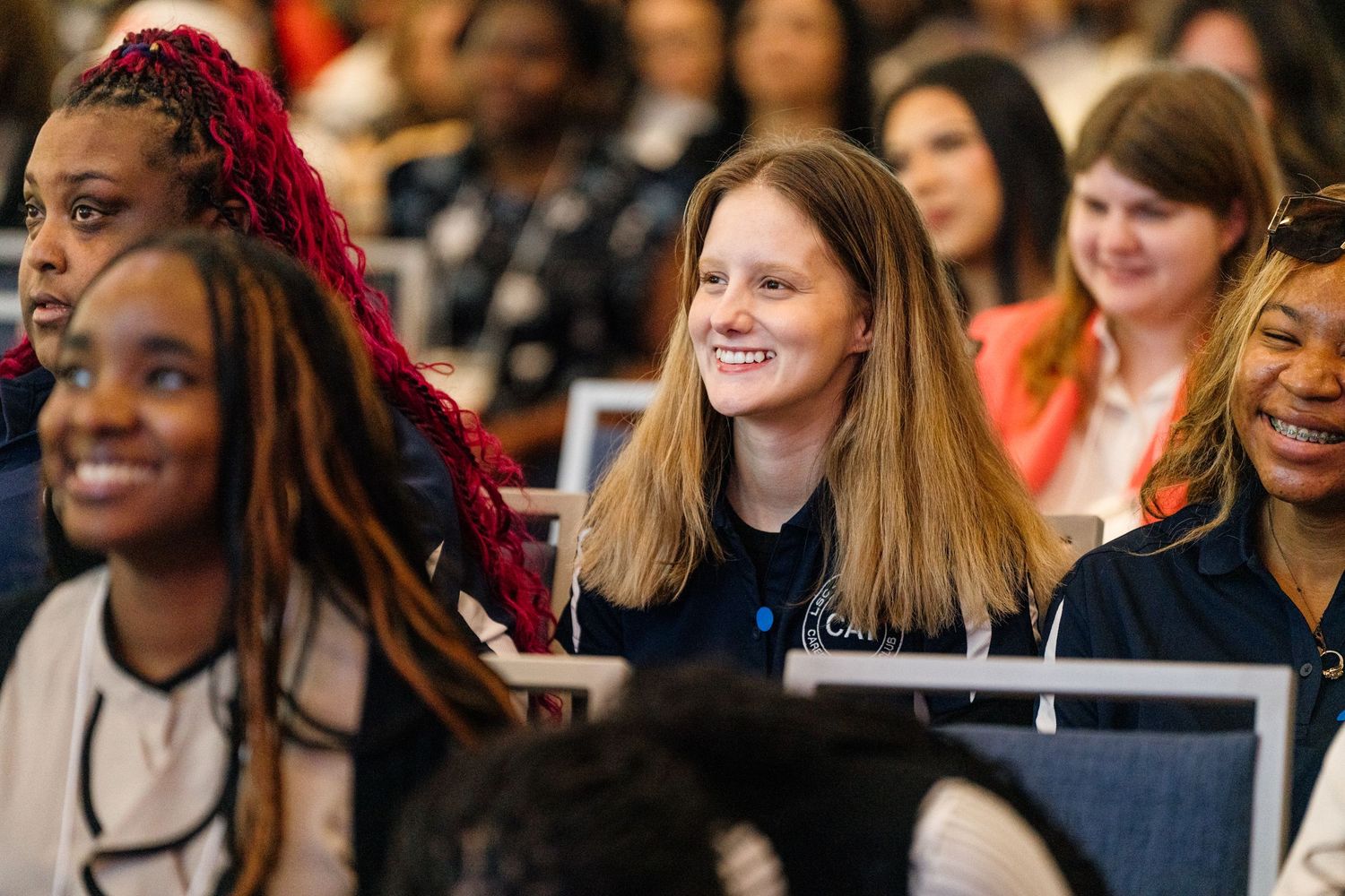 Diverse group of smiling women attending a conference or seminar, engaged and happy in a professional setting.