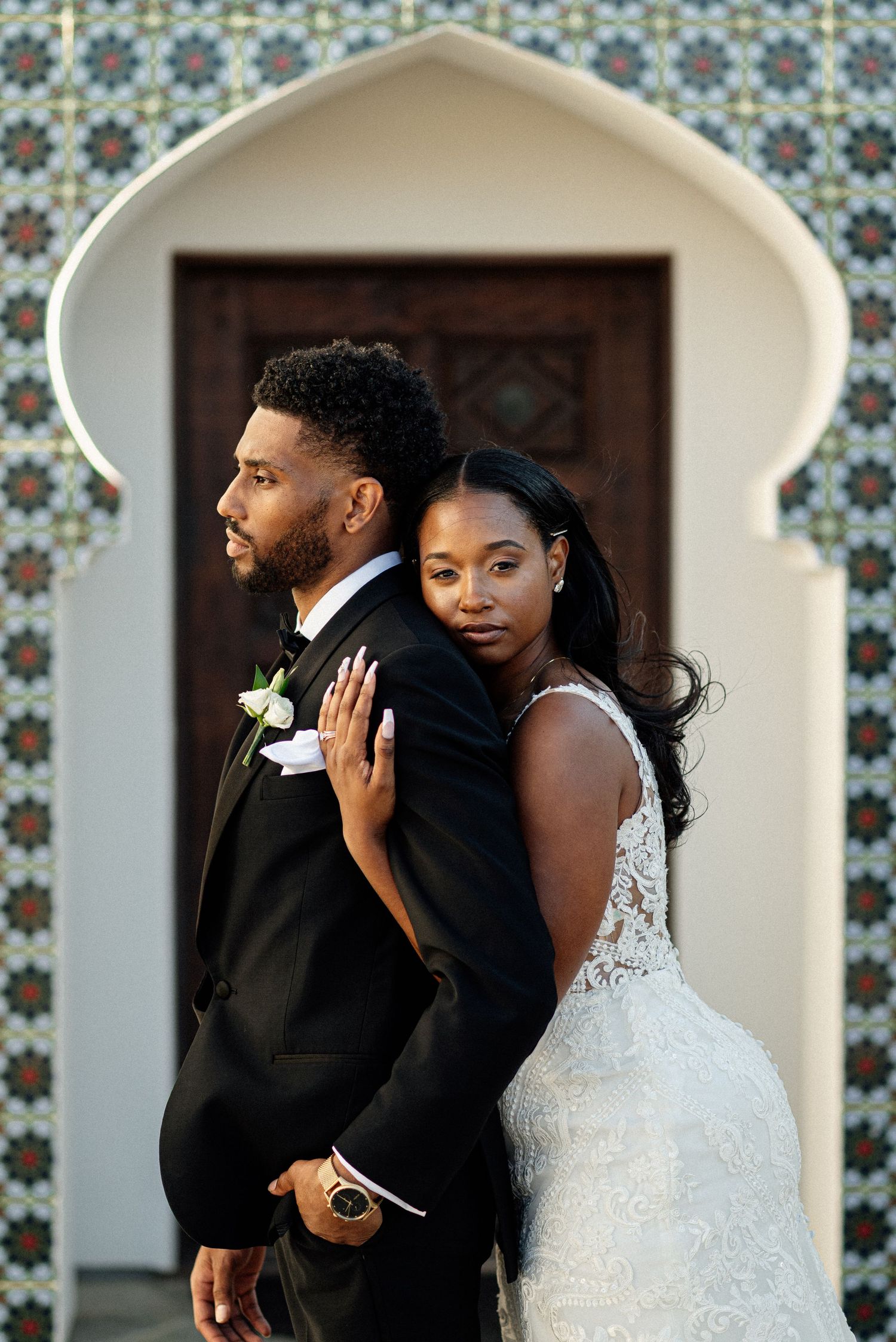A stylish wedding portrait against a decorative tiled wall with an arched doorway.