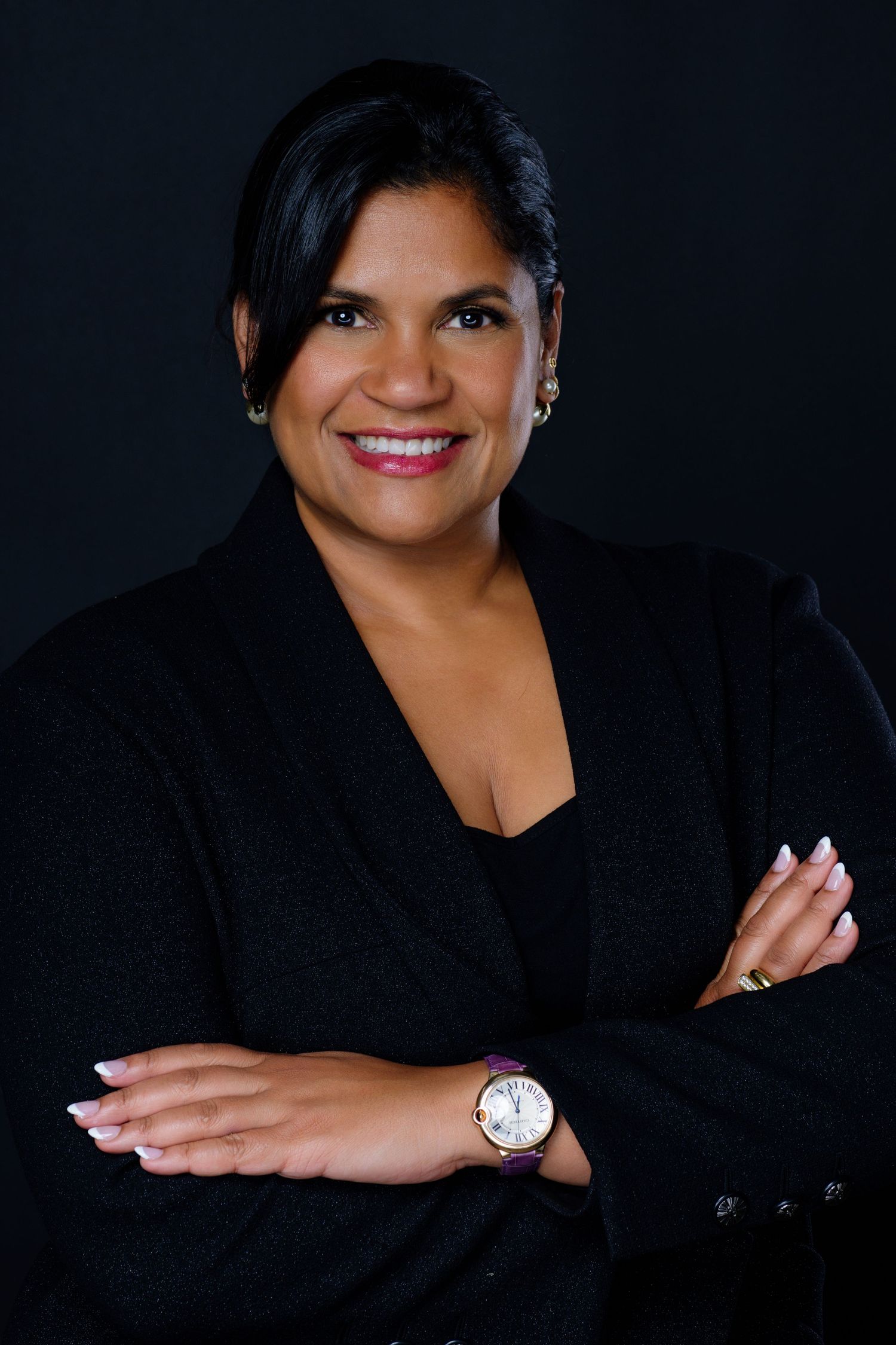 Professional portraits of someone in black blazer with silver watch against dark background.
