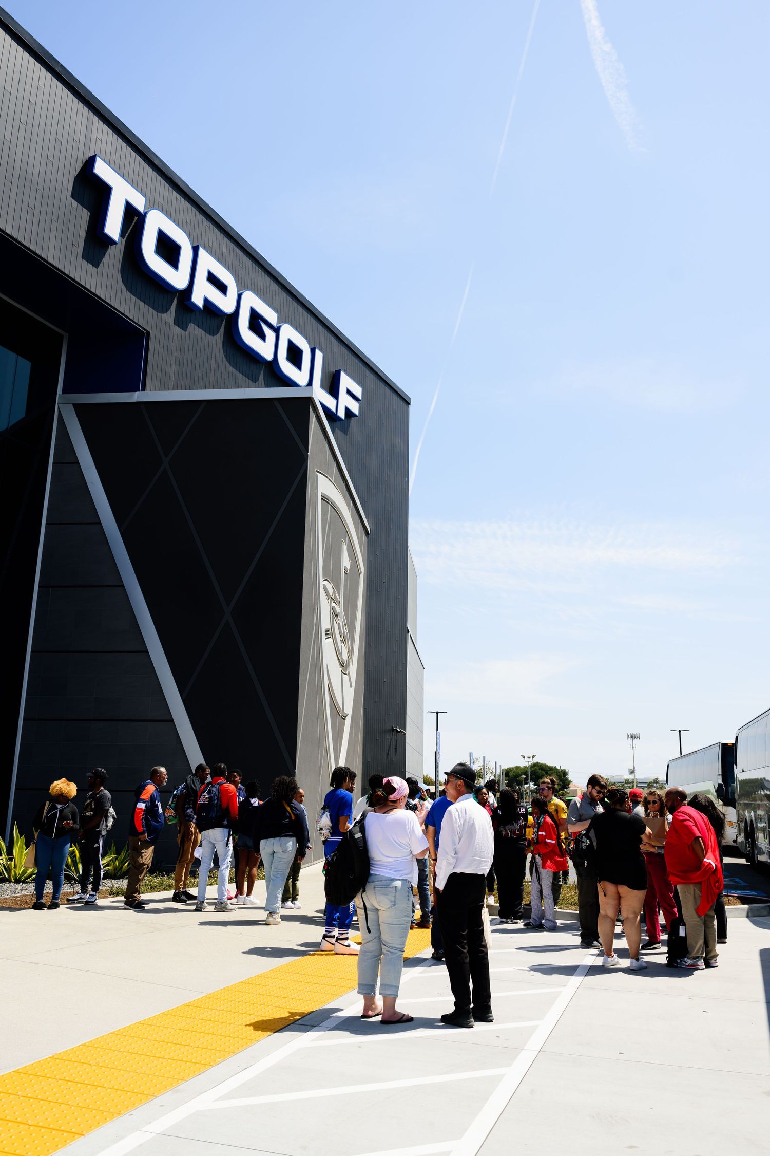 People gathering outside a modern black building with yellow walkway under blue sky.