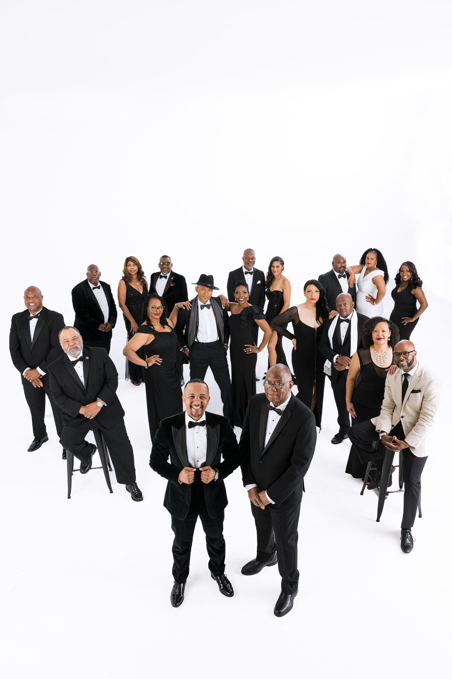 Large group of people in formal black and white attire posed against white background.