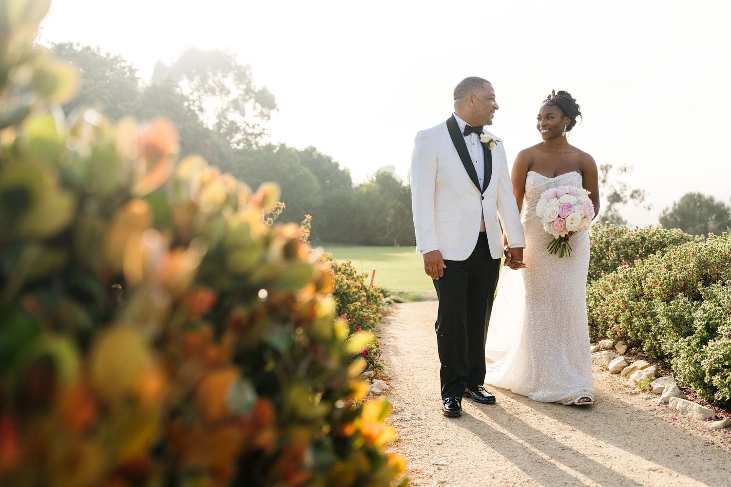 Romantic wedding couple poses in a sun-drenched garden setting during golden hour.