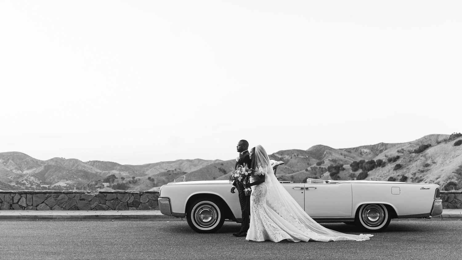 Classic vintage car and wedding dress silhouettes against mountain landscape.