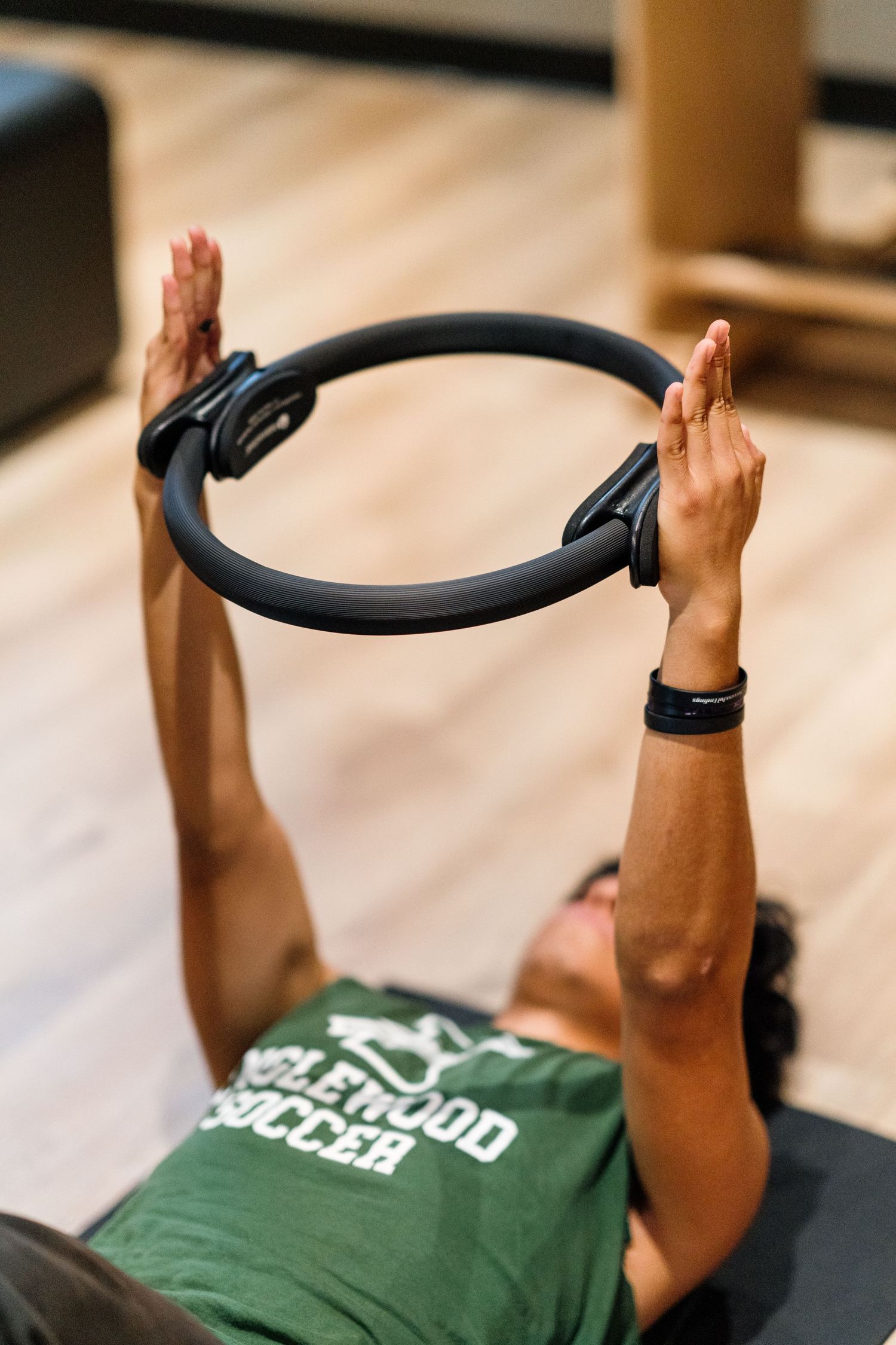 Person exercising with a Pilates ring while wearing a green workout shirt.
