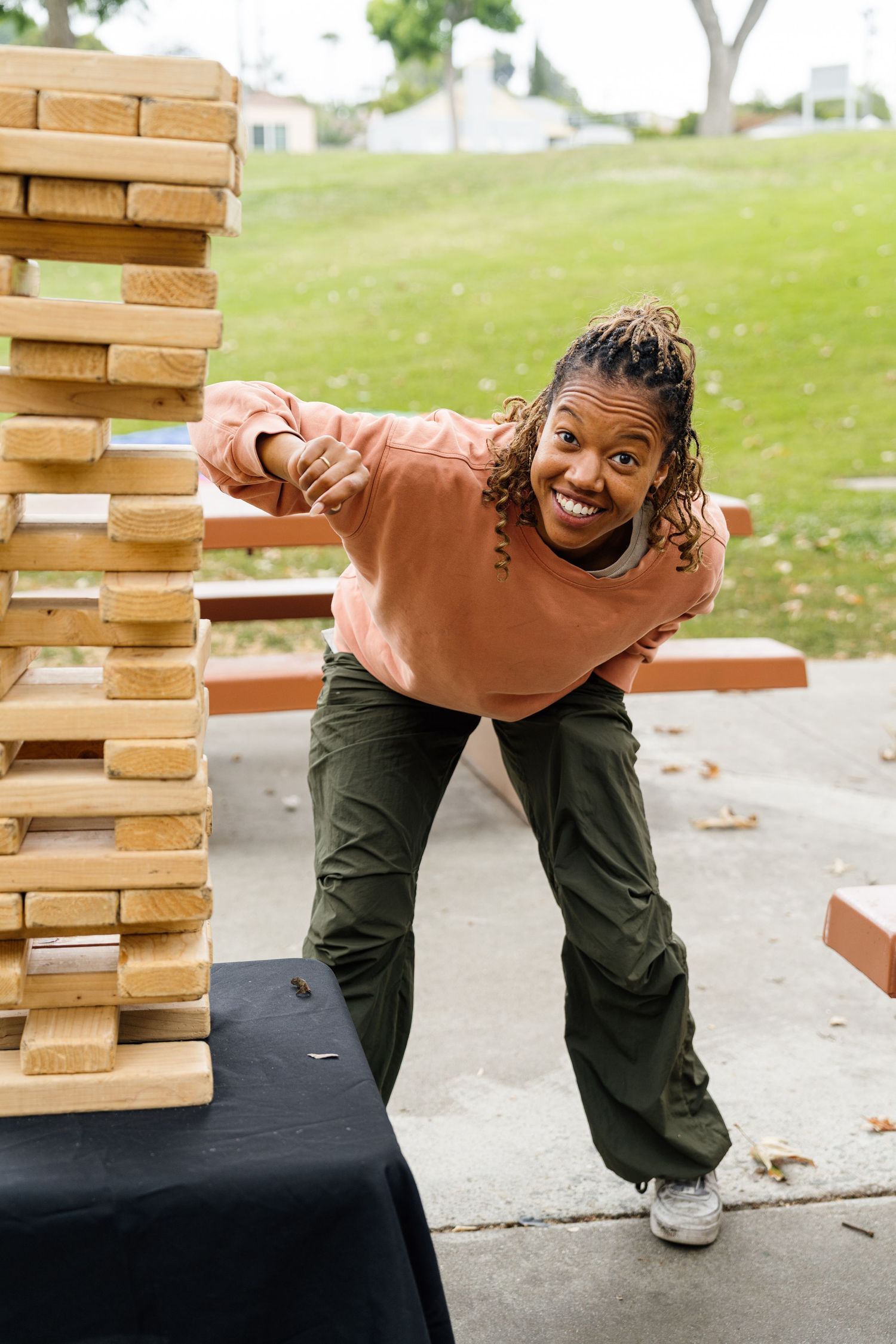 Person playing giant Jenga game outdoors on a sunny day.
