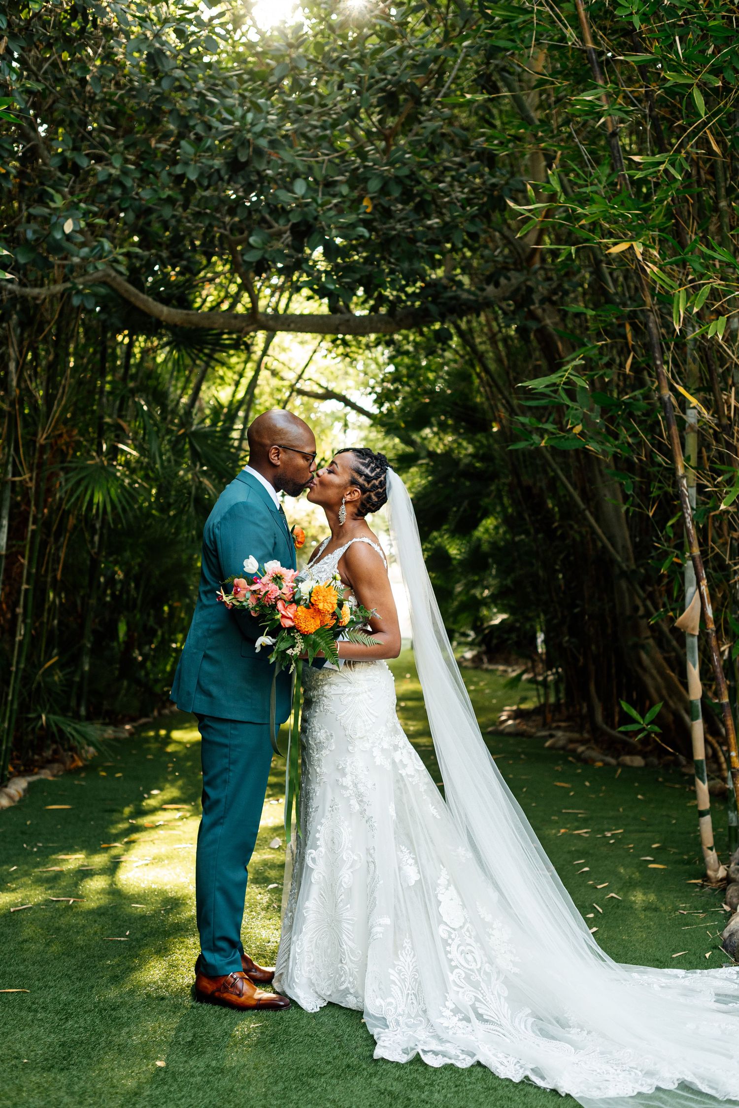 A wedding couple sharing a romantic moment under a natural bamboo archway in a garden setting.