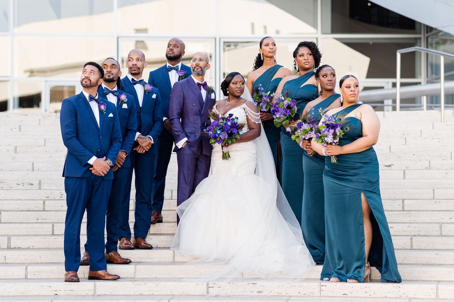 Wedding party in blue and green attire poses on modern concrete steps.