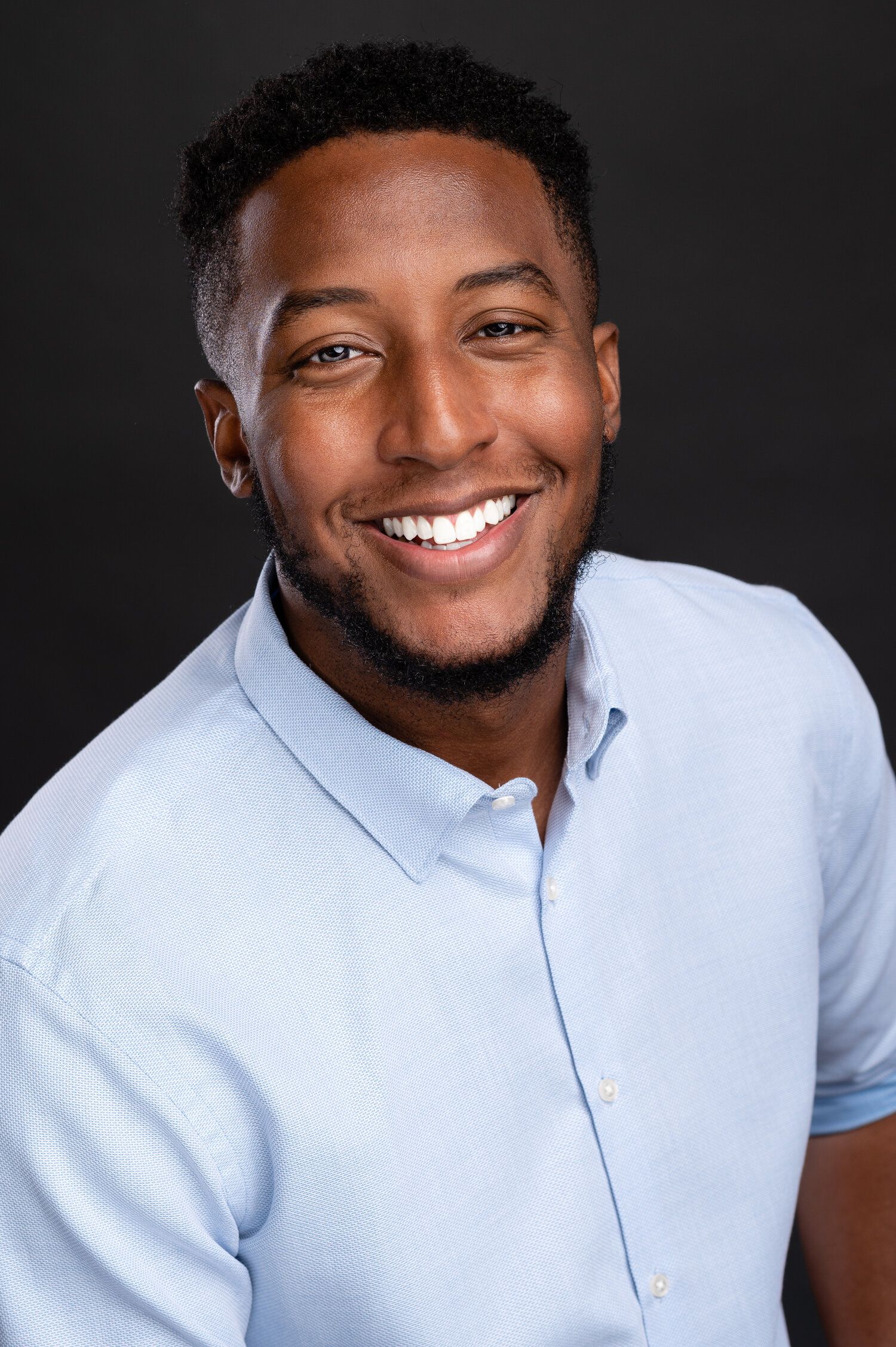 Portrait series showing joyful expressions while wearing light blue button-down shirt against dark background.