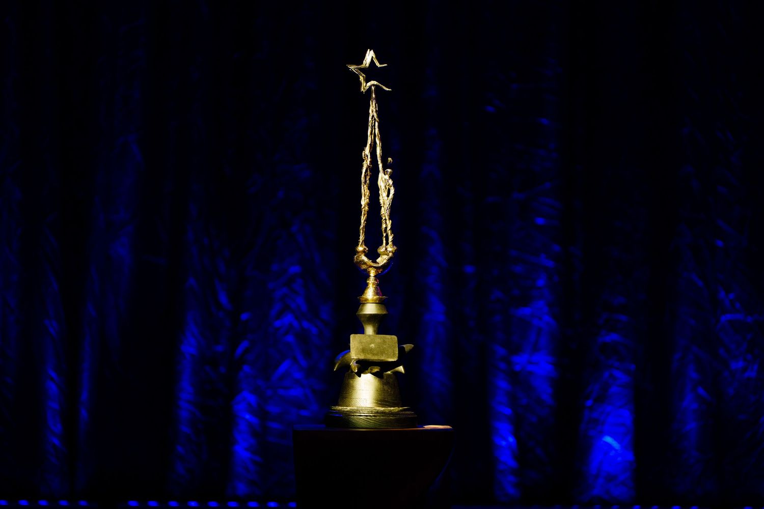 Silhouettes of golden trophy or award figures against dark blue background.