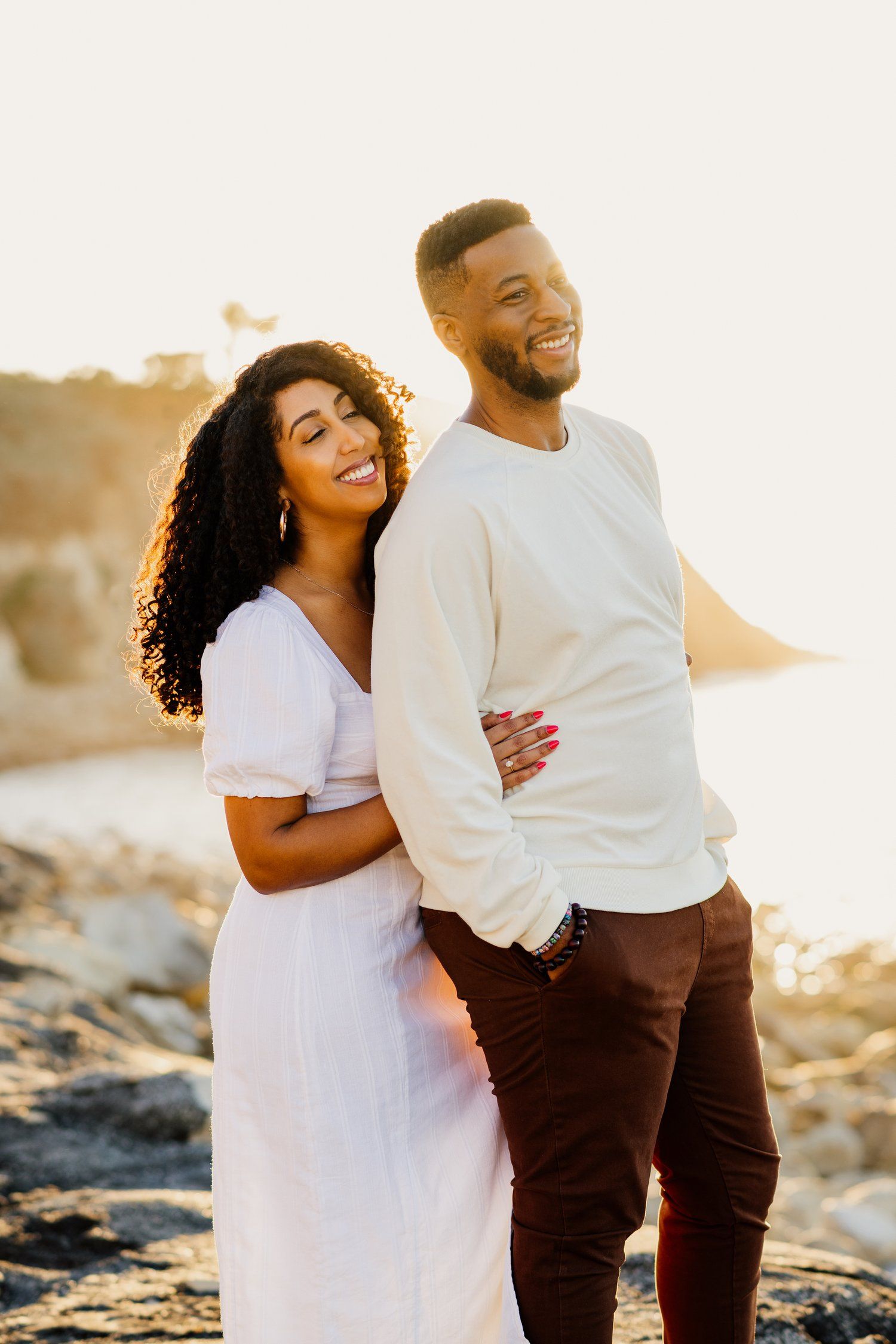 Couple in white shirts laughing together on beach at sunset.