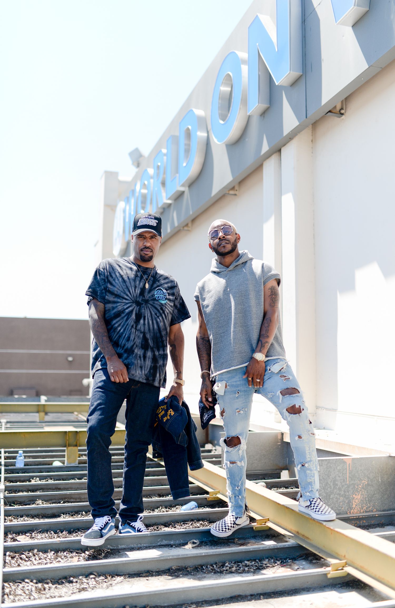 Two people sitting casually on concrete steps wearing casual streetwear and sneakers.