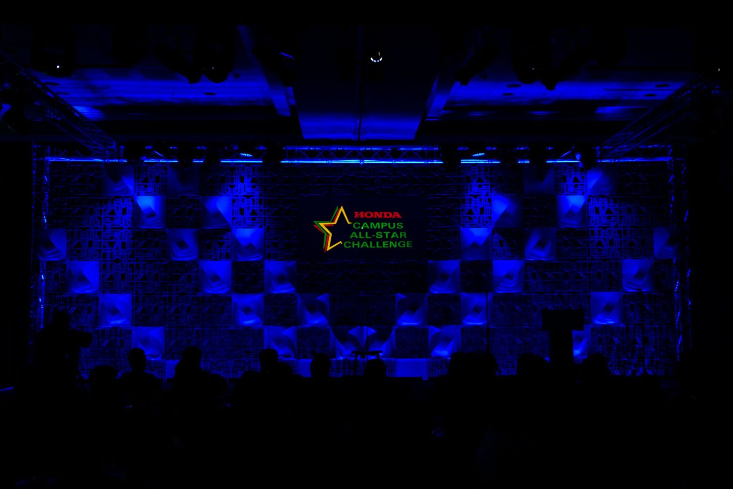 Dark stage with blue lighting and geometric pattern backdrop for an event.