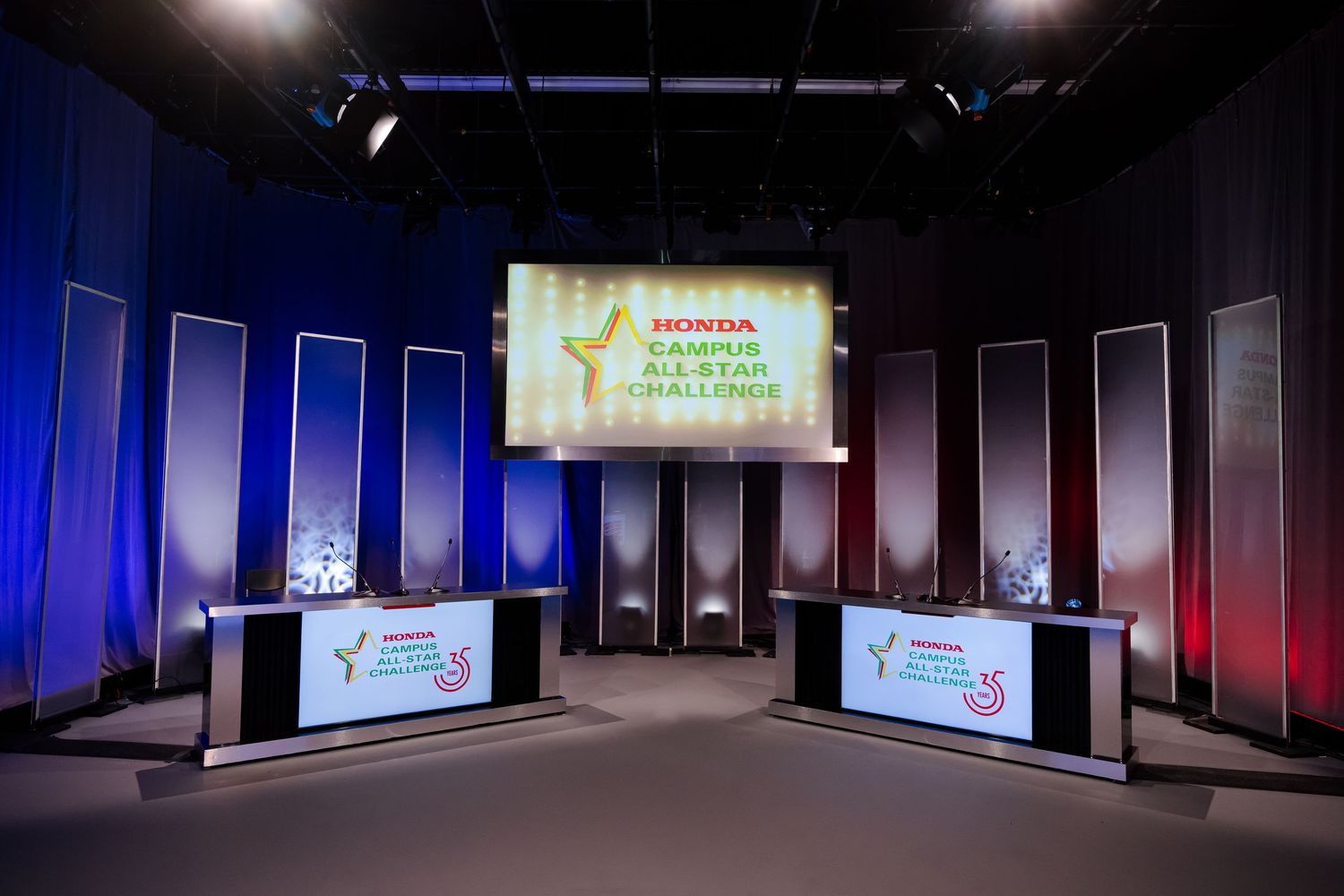 Dark auditorium stage with multiple screens displaying Campus All-Star Challenge logos.