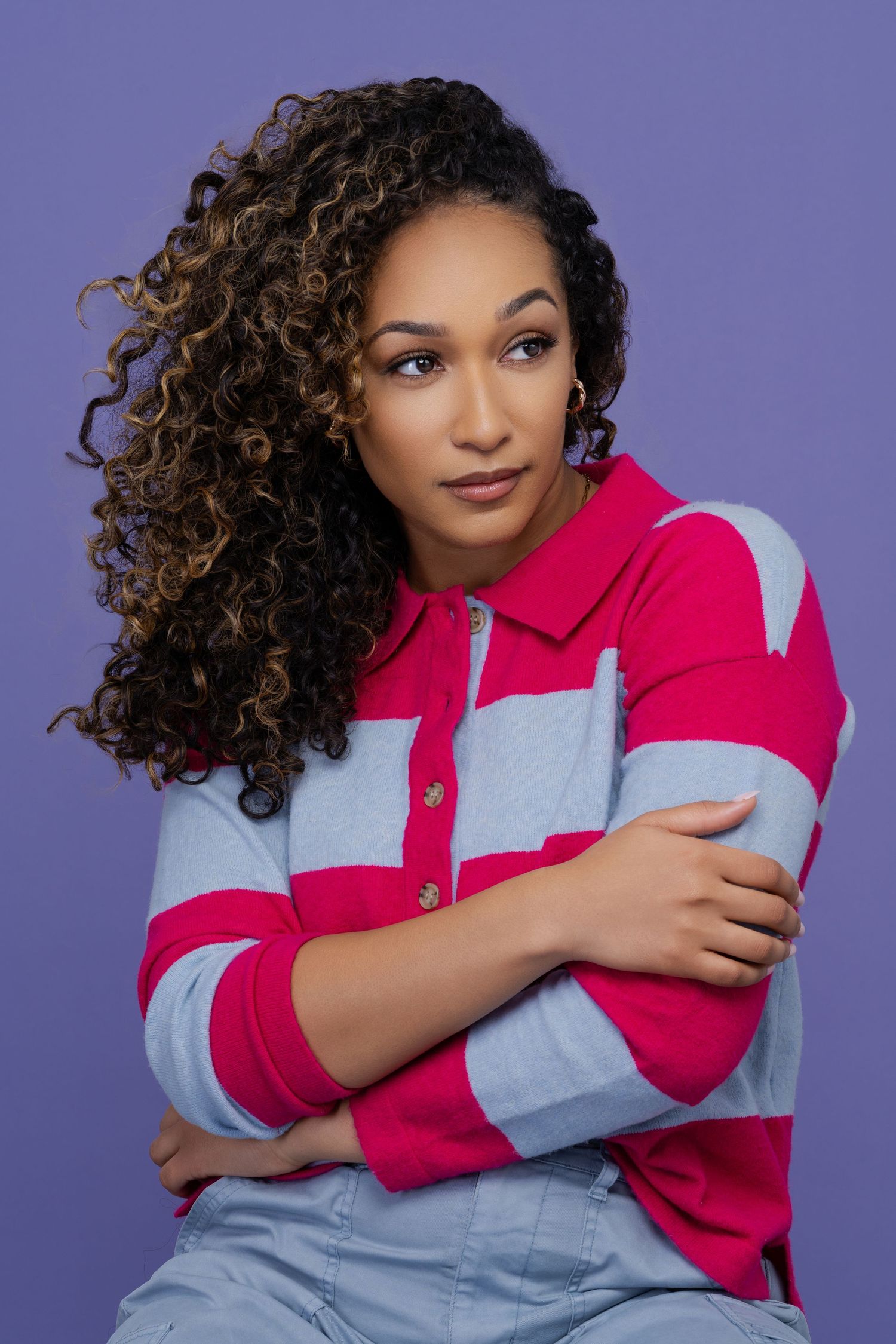 Model in pink and gray color block shirt poses confidently against purple background.