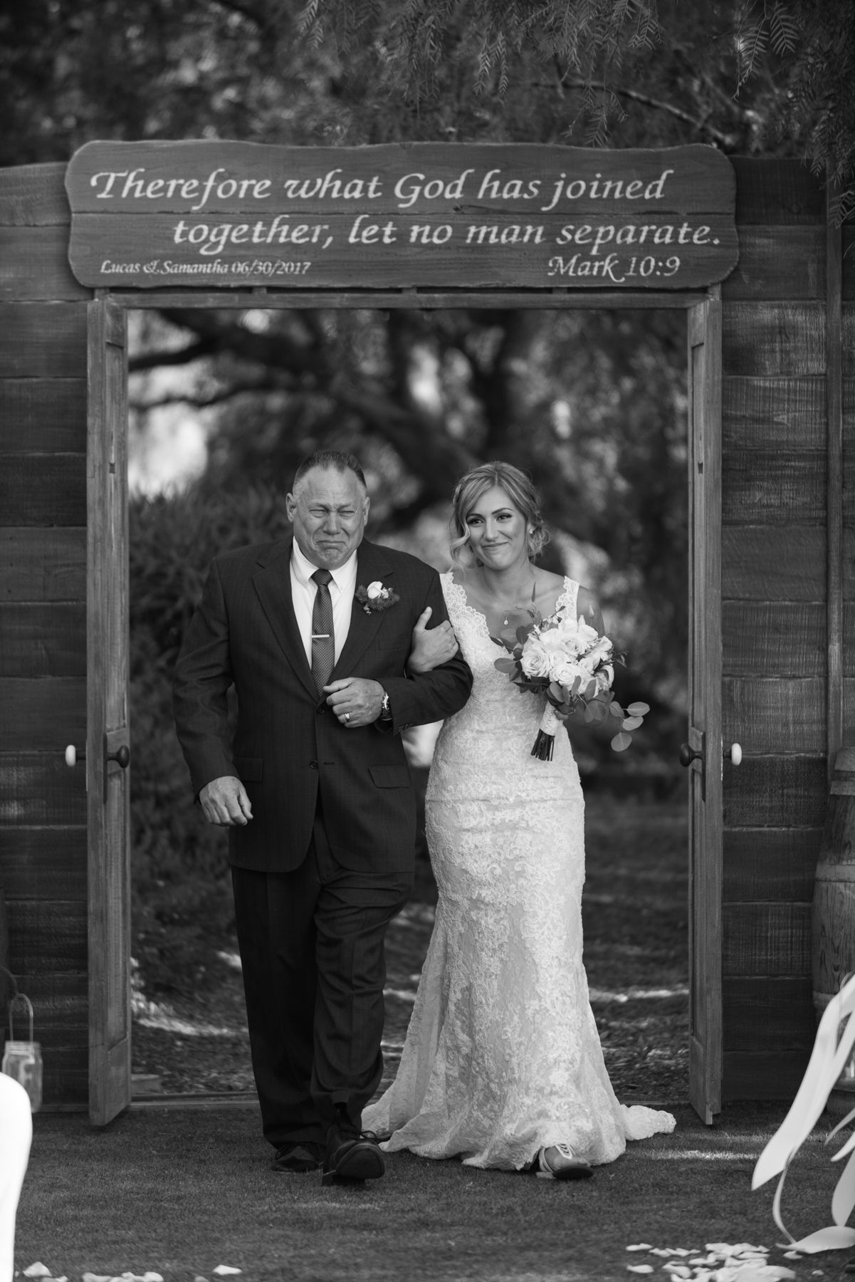 A wedding entrance arch displays a Bible verse from Mark 10:9 as a couple walks beneath it.