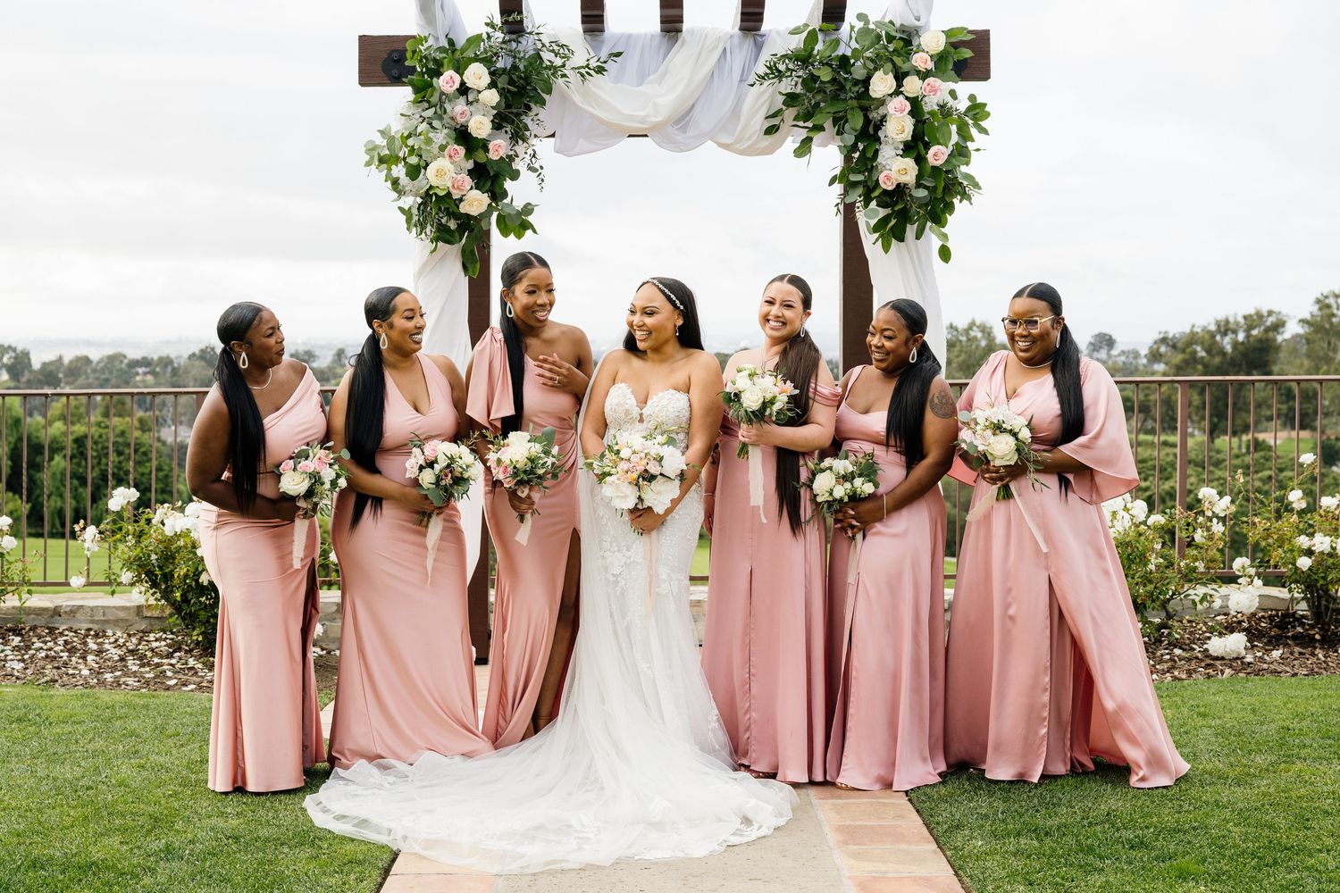 Wedding party in pink bridesmaid dresses and white bridal gown posing outdoors.