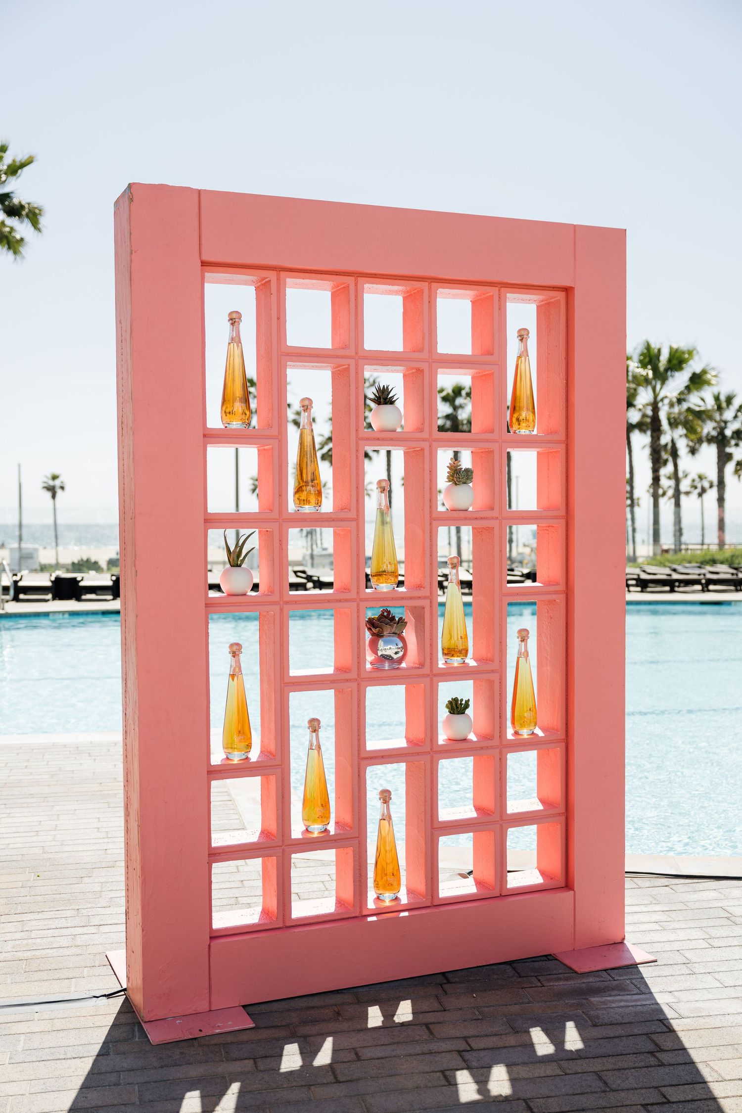 Pink display wall with illuminated bottle shelves on a beachfront deck.