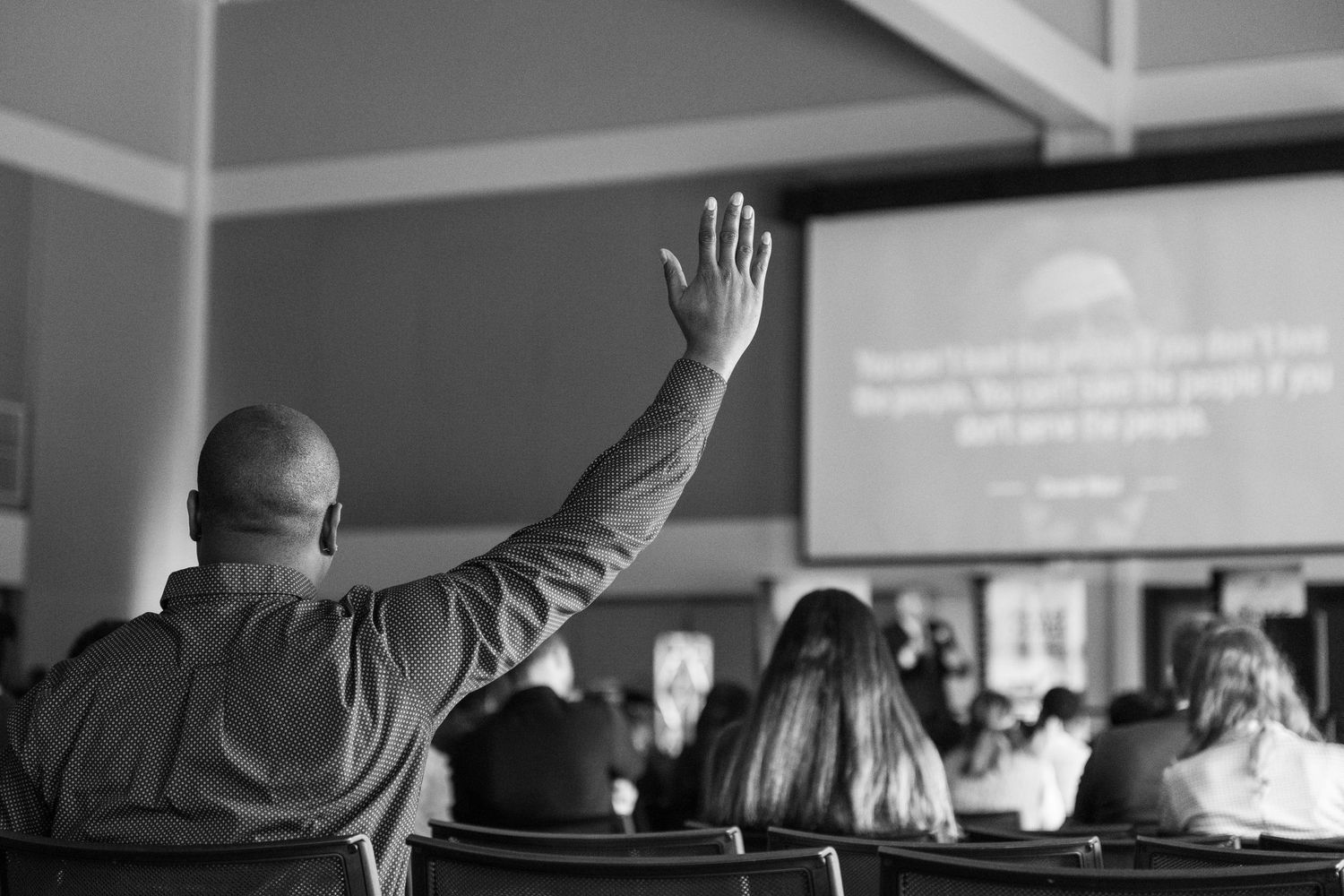 Black and white photo of someone raising their hand during a conference presentation.