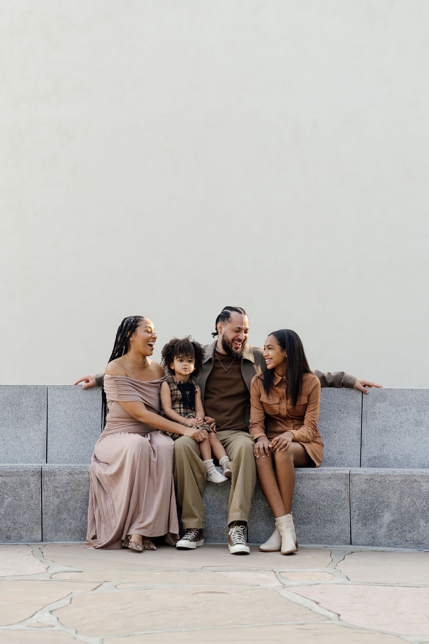 Family shares joyful moments while sitting together on a stone bench during a casual photoshoot.
