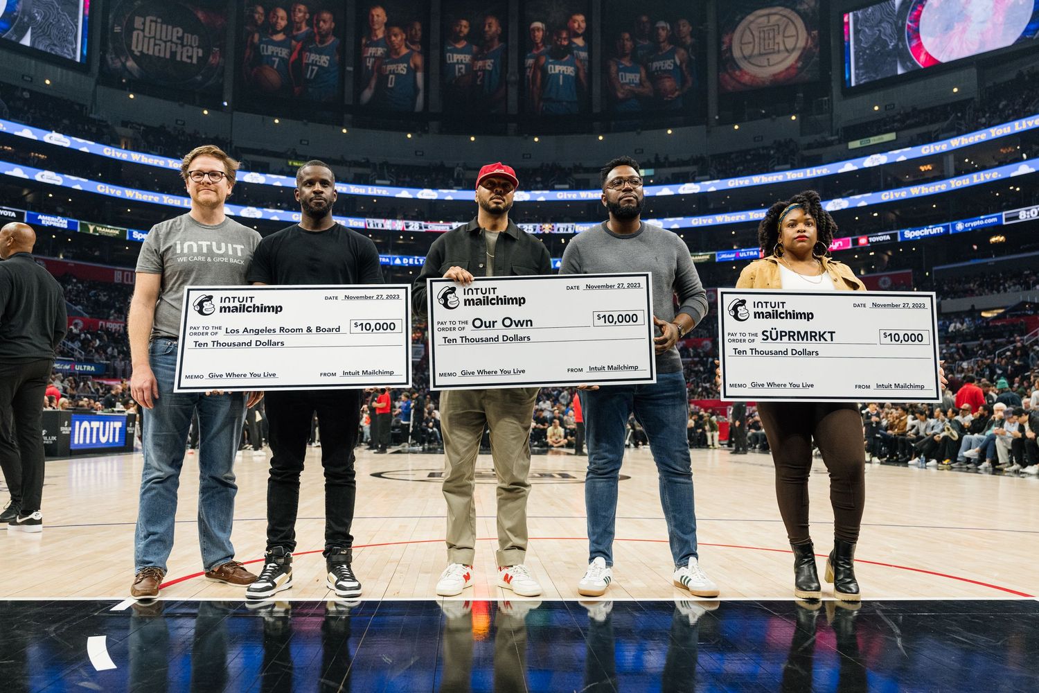 Large indoor sports arena with people standing on court holding oversized checks.