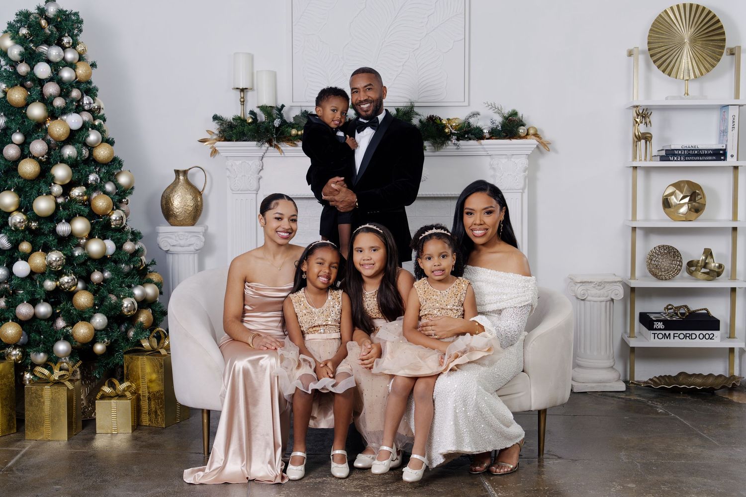 Family poses together in coordinated outfits for holiday photos with a decorated Christmas tree.