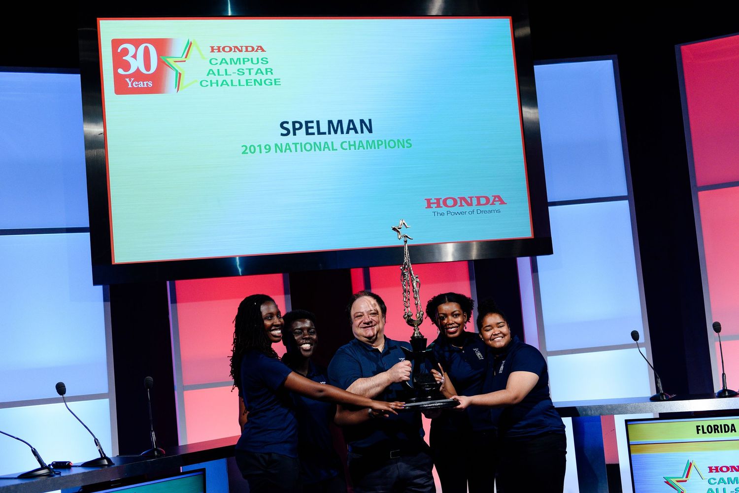 Conference stage setup with multiple digital displays showing Spelman branding.