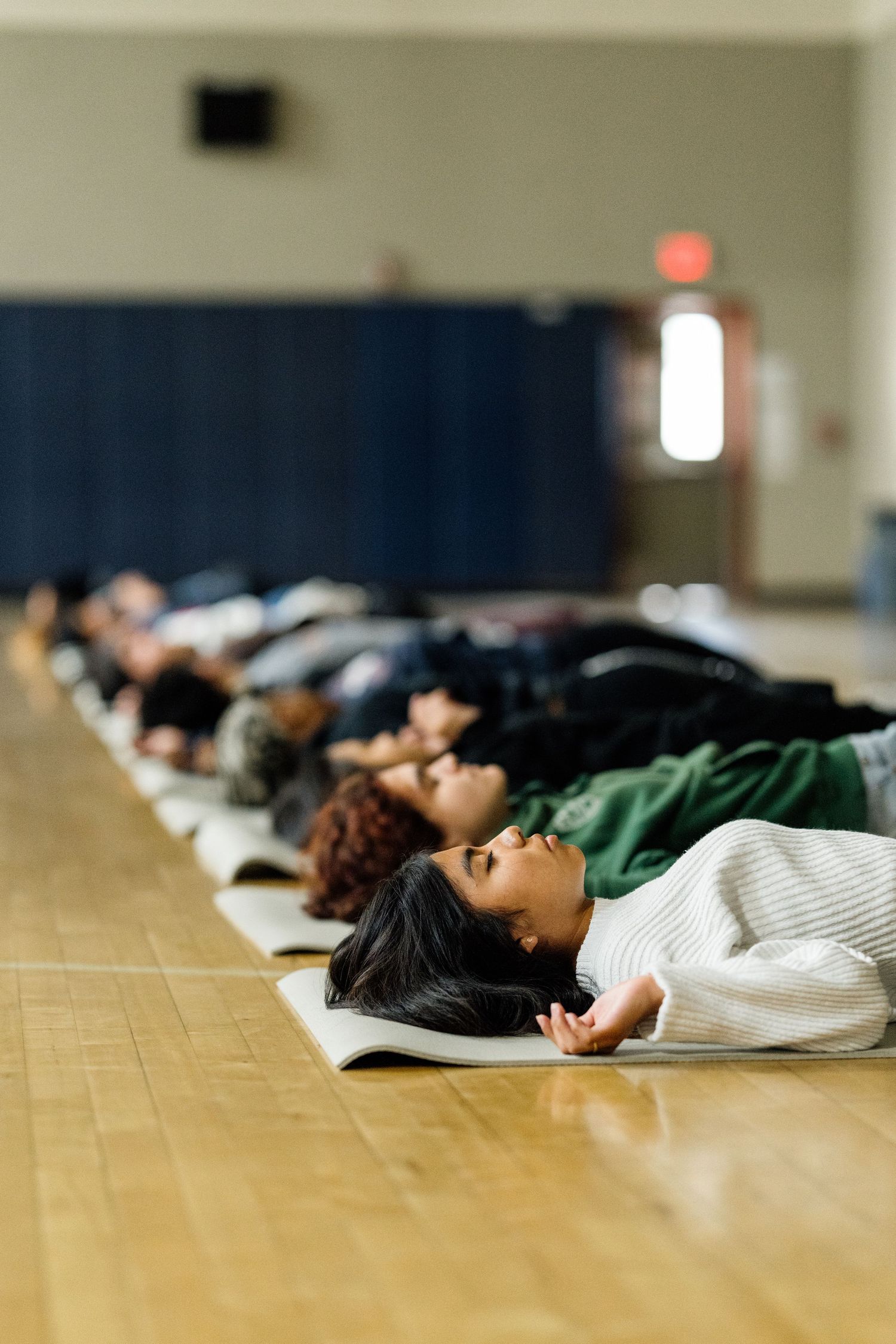 People lying on wooden floor in a row during an indoor activity.