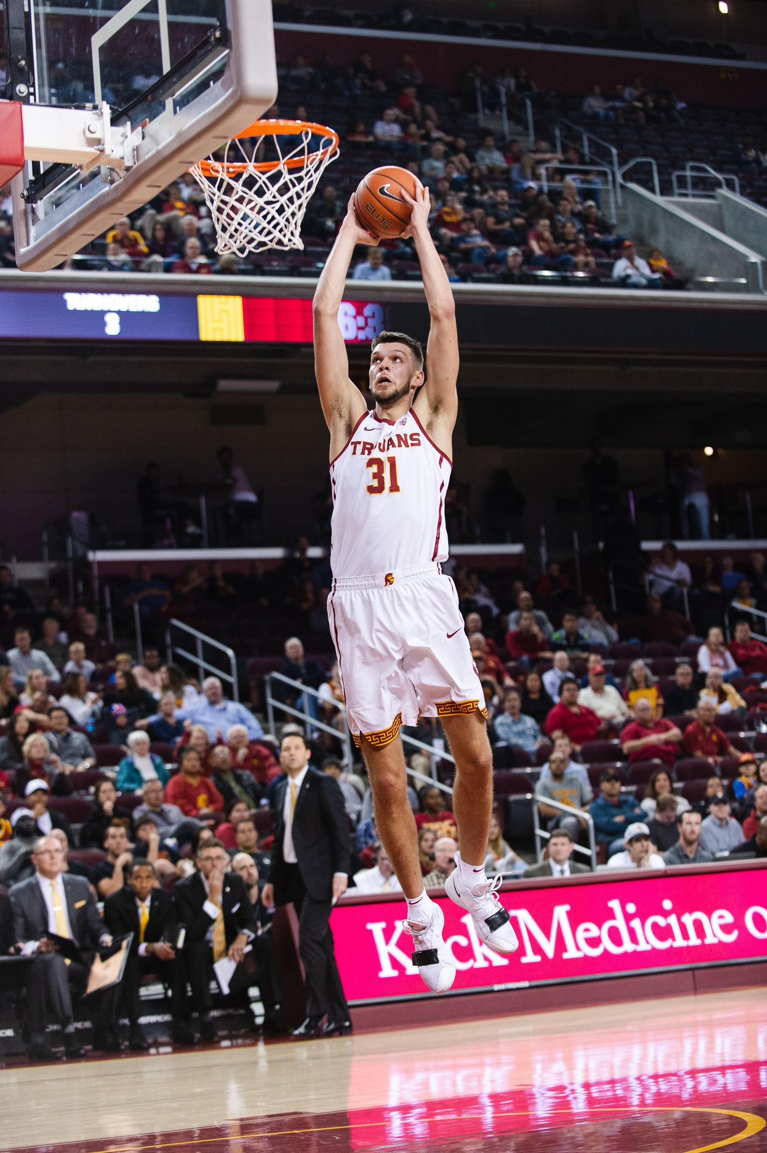 Basketball player in white jersey dunks ball during indoor game.