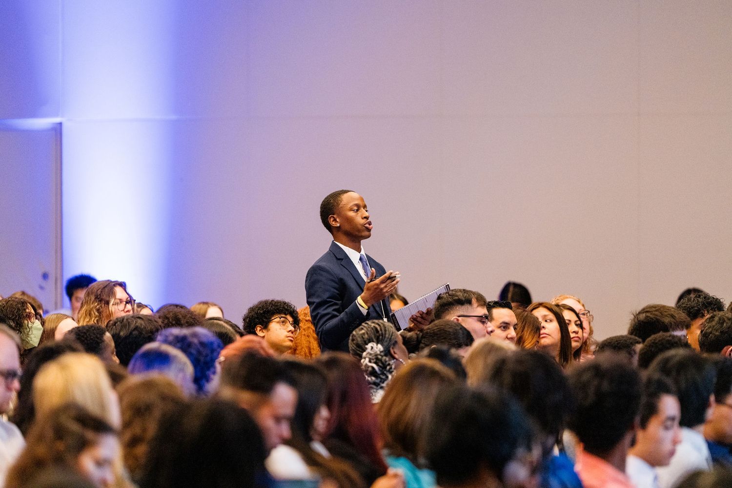 Large audience seated in rows at a conference with blue stage lighting.