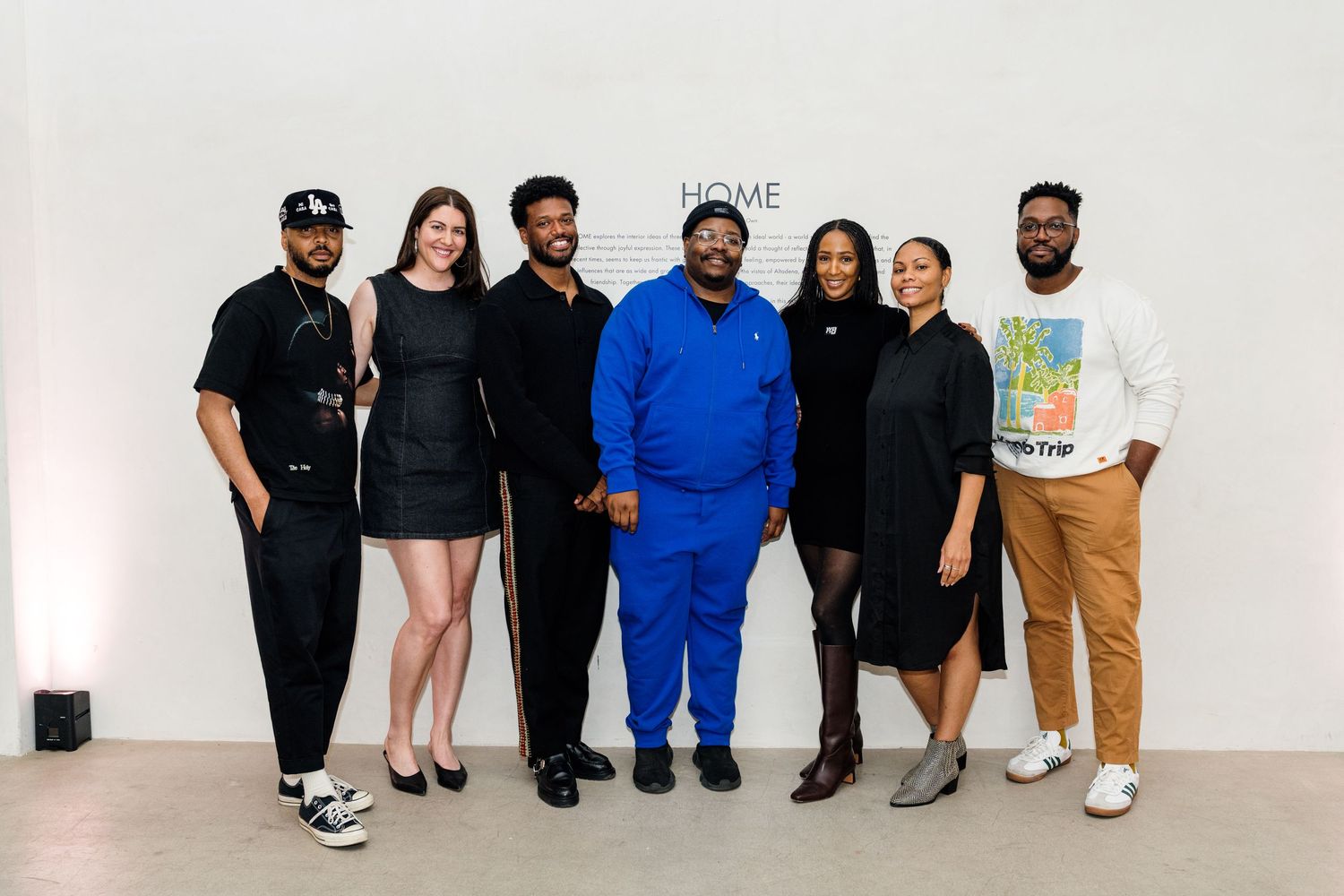A group of people standing together against a white wall wearing casual clothing.