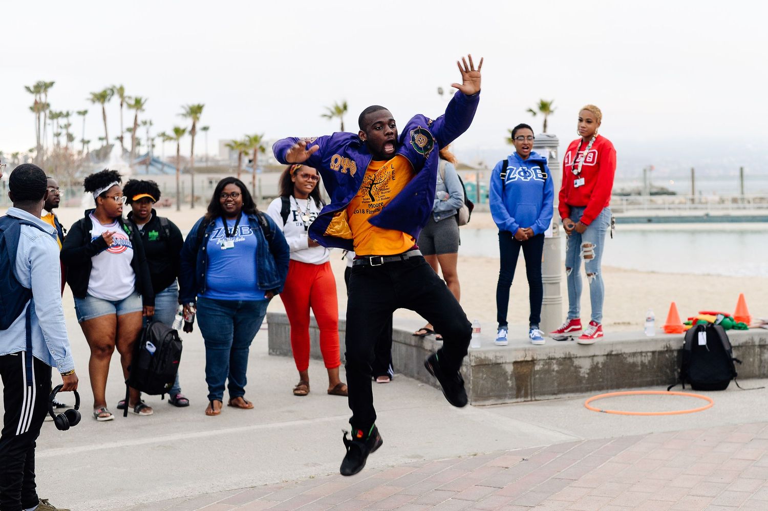 People performing synchronized jumping poses outdoors near palm trees and beach.