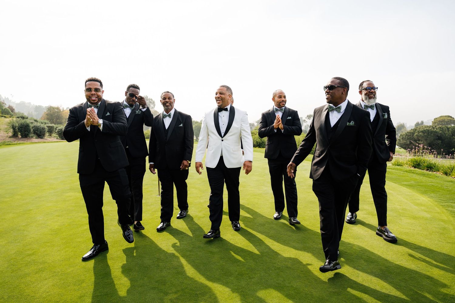Groomsmen in formal attire walking across sunny green golf course.