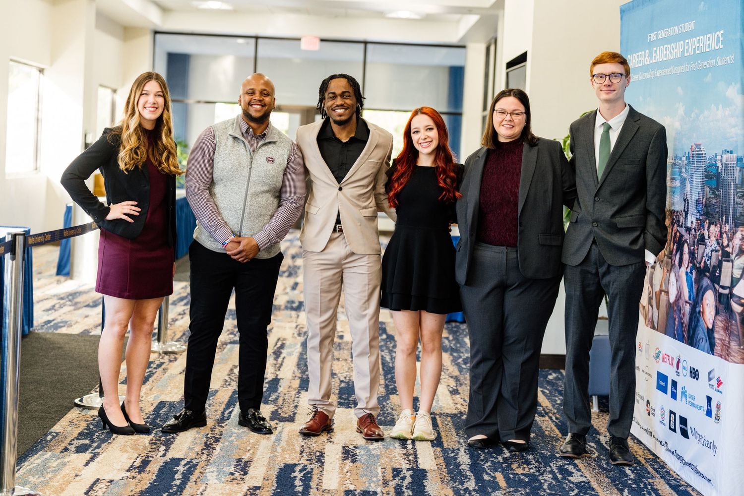 Six young professionals smiling together in a hallway at a business networking event.
