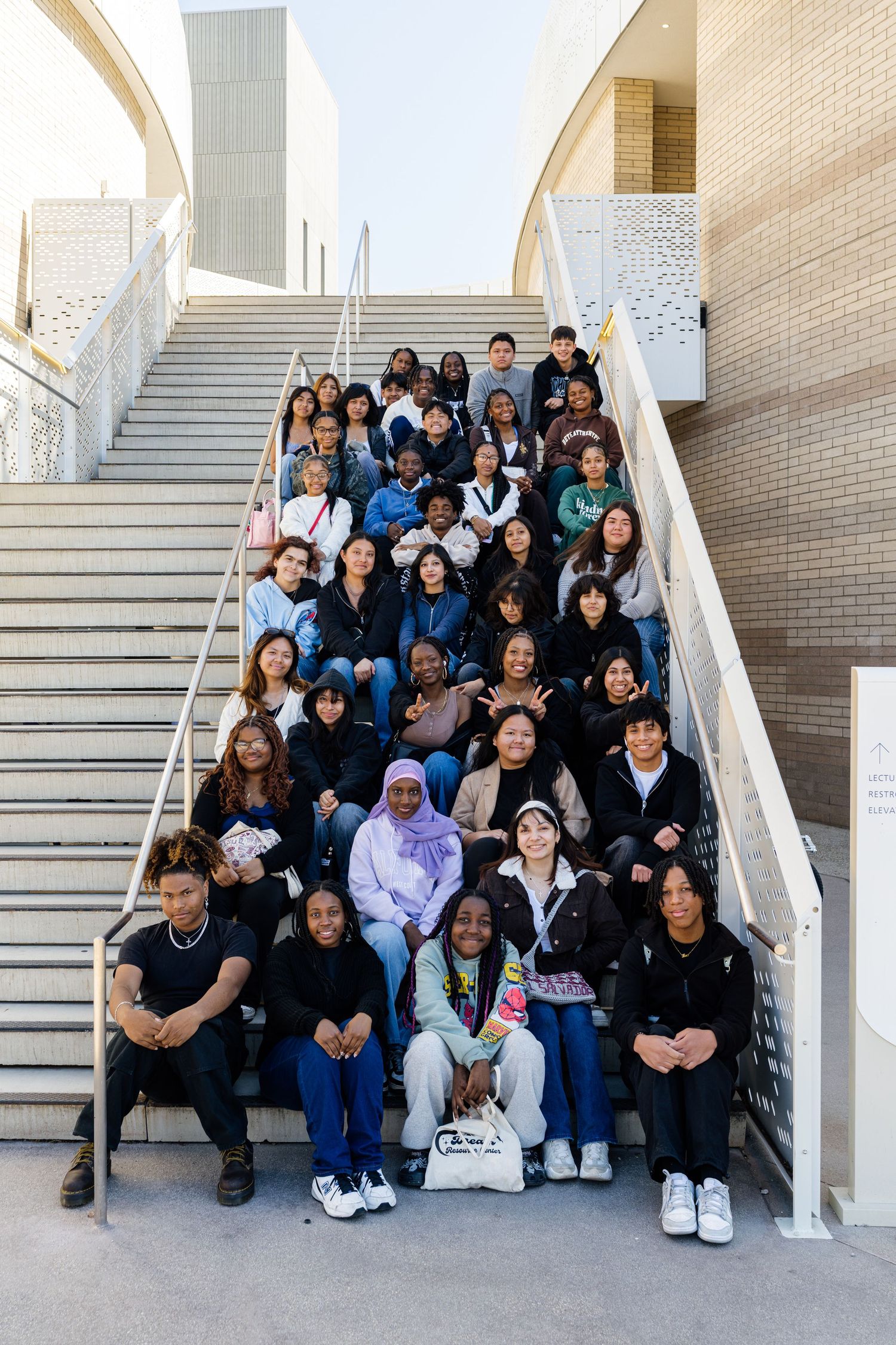 Large group seated on concrete steps in architectural setting.