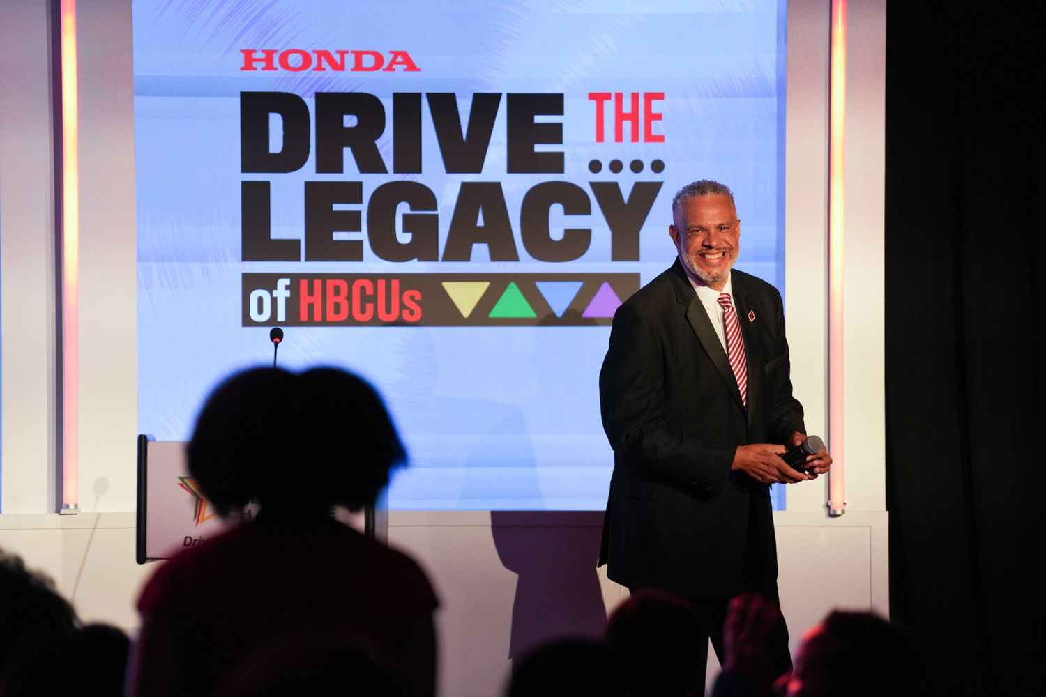 Man presenting at Honda Drive the Legacy of HBCUs event on stage with large branded screen backdrop.