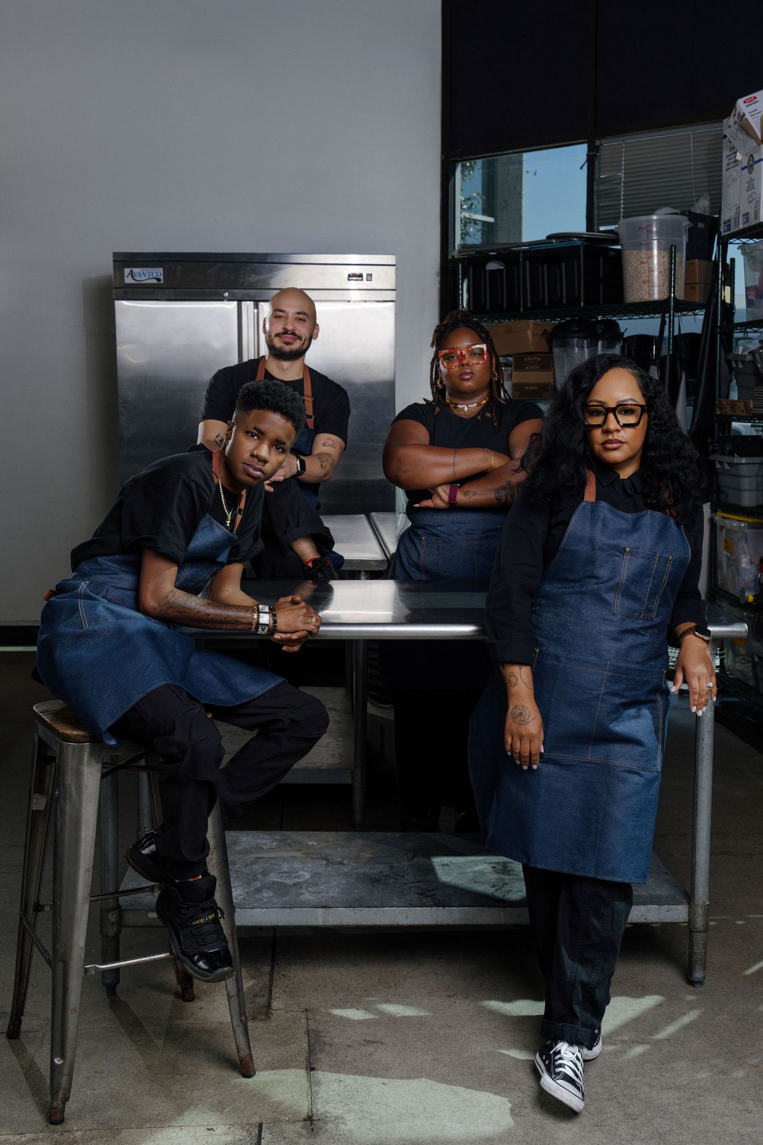 Four kitchen staff in denim aprons pose confidently in a professional restaurant kitchen setting.