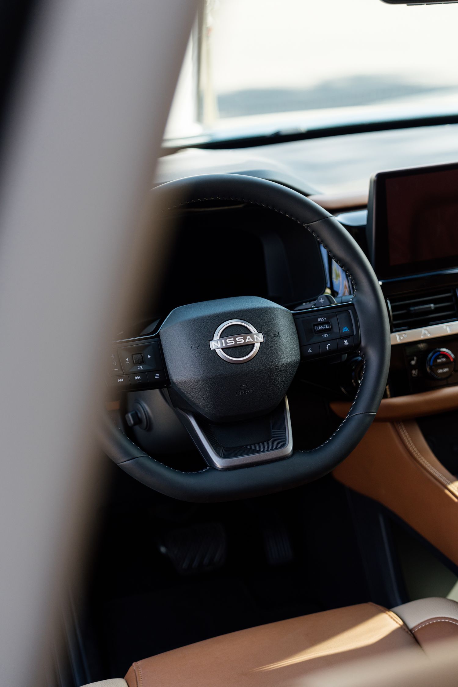 Nissan vehicle interior featuring a black leather steering wheel with Nissan logo and tan leather seats.