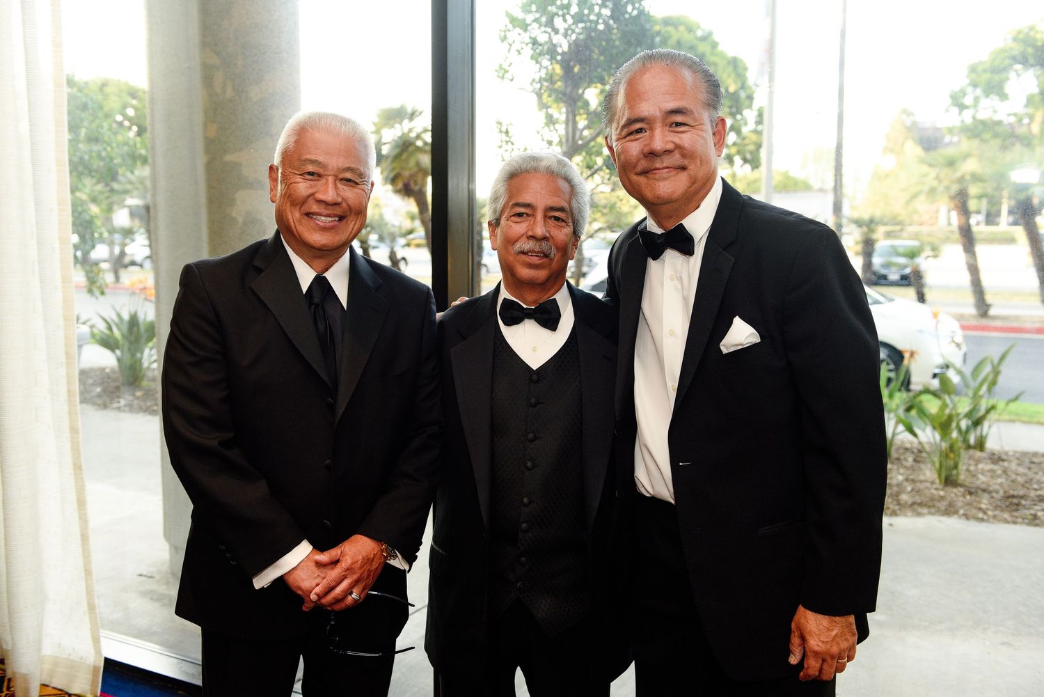 Formal group photo of people wearing black tie attire in bright venue.
