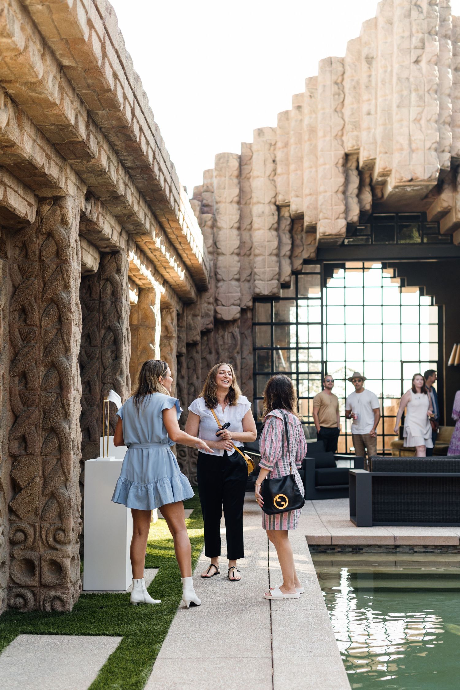 Stone pillared venue with reflecting pool and guests mingling in an elegant outdoor space.