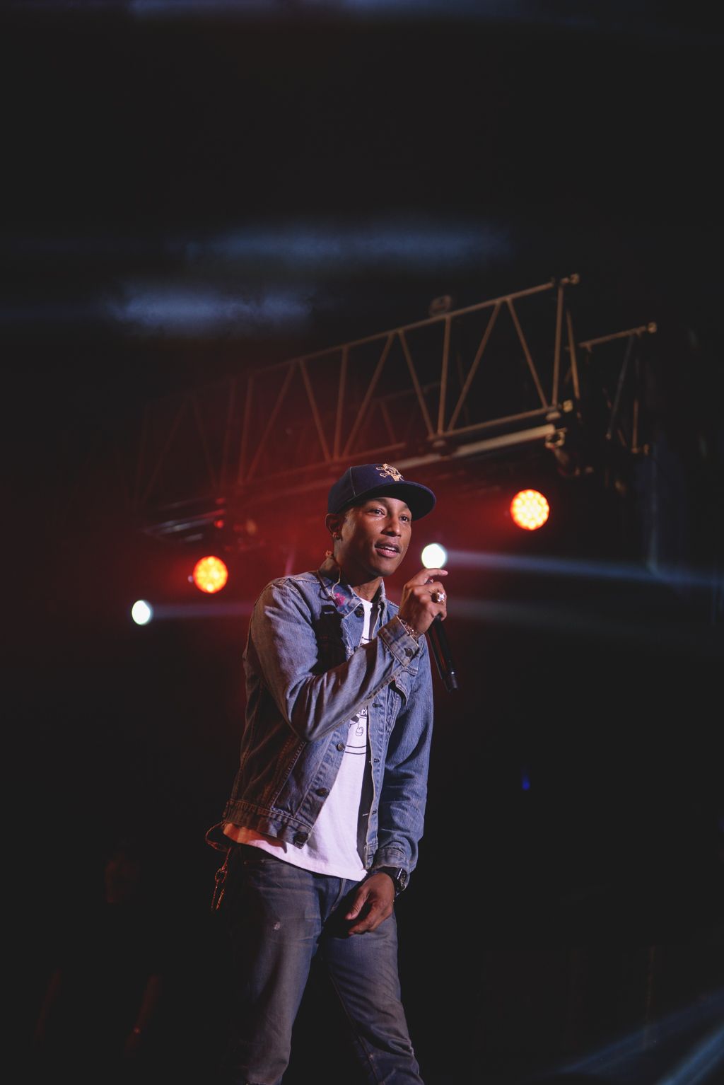 Performer in denim jacket and hat singing on stage with dramatic lighting.