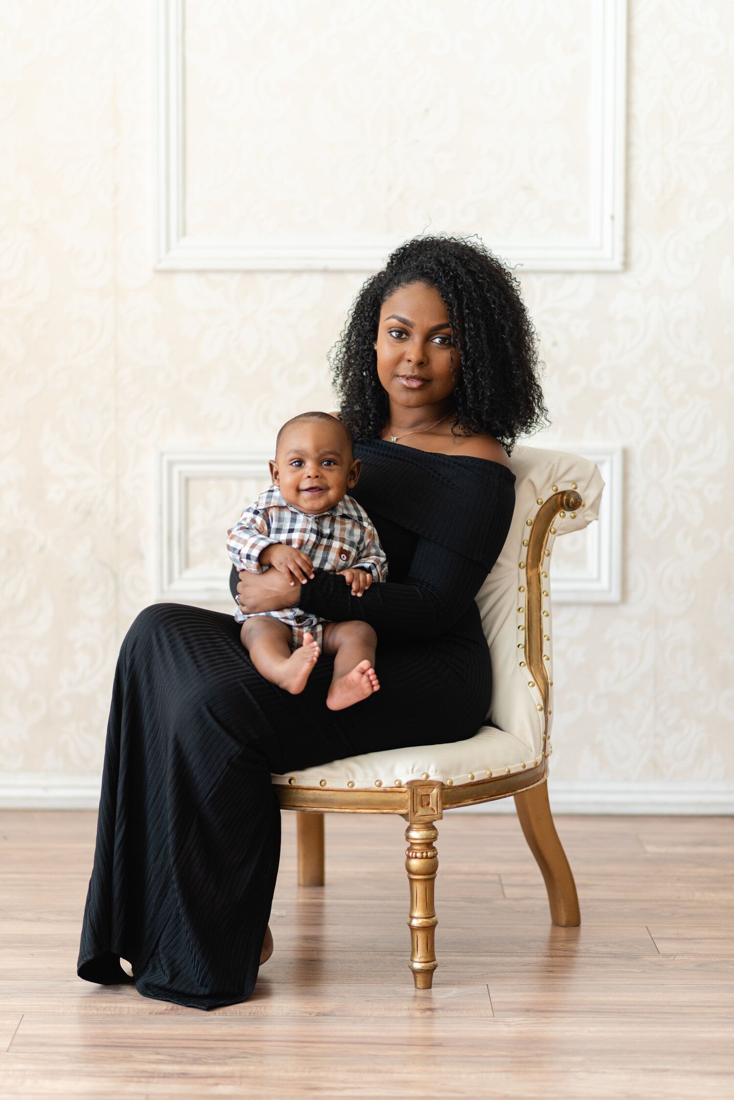Parent and baby in matching black outfits sitting in elegant gold chair.