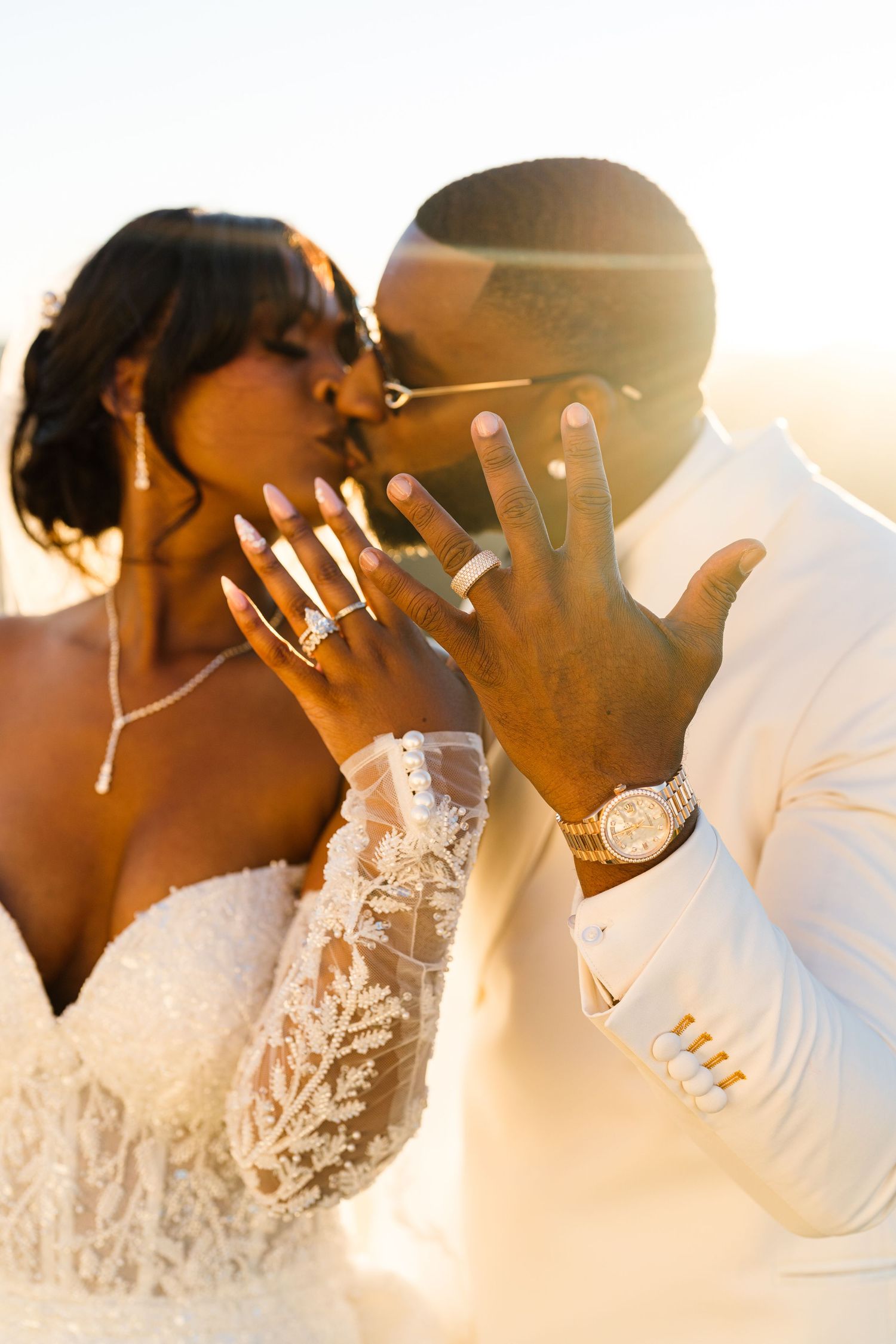 Close-up of newlyweds' hands showing off their wedding rings in golden sunlight.