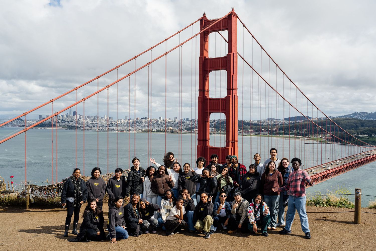 Group of tourists posing in front of the iconic Golden Gate Bridge in San Francisco on a cloudy day.