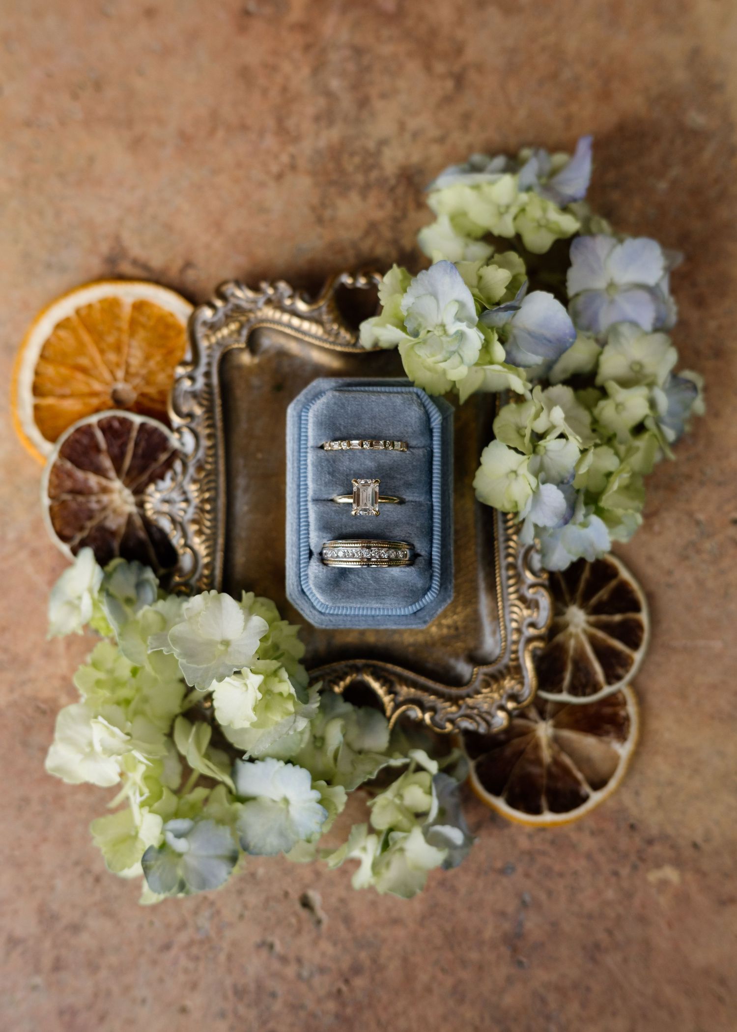 Wedding rings displayed in a vintage box with dried orange slices and hydrangea flowers.