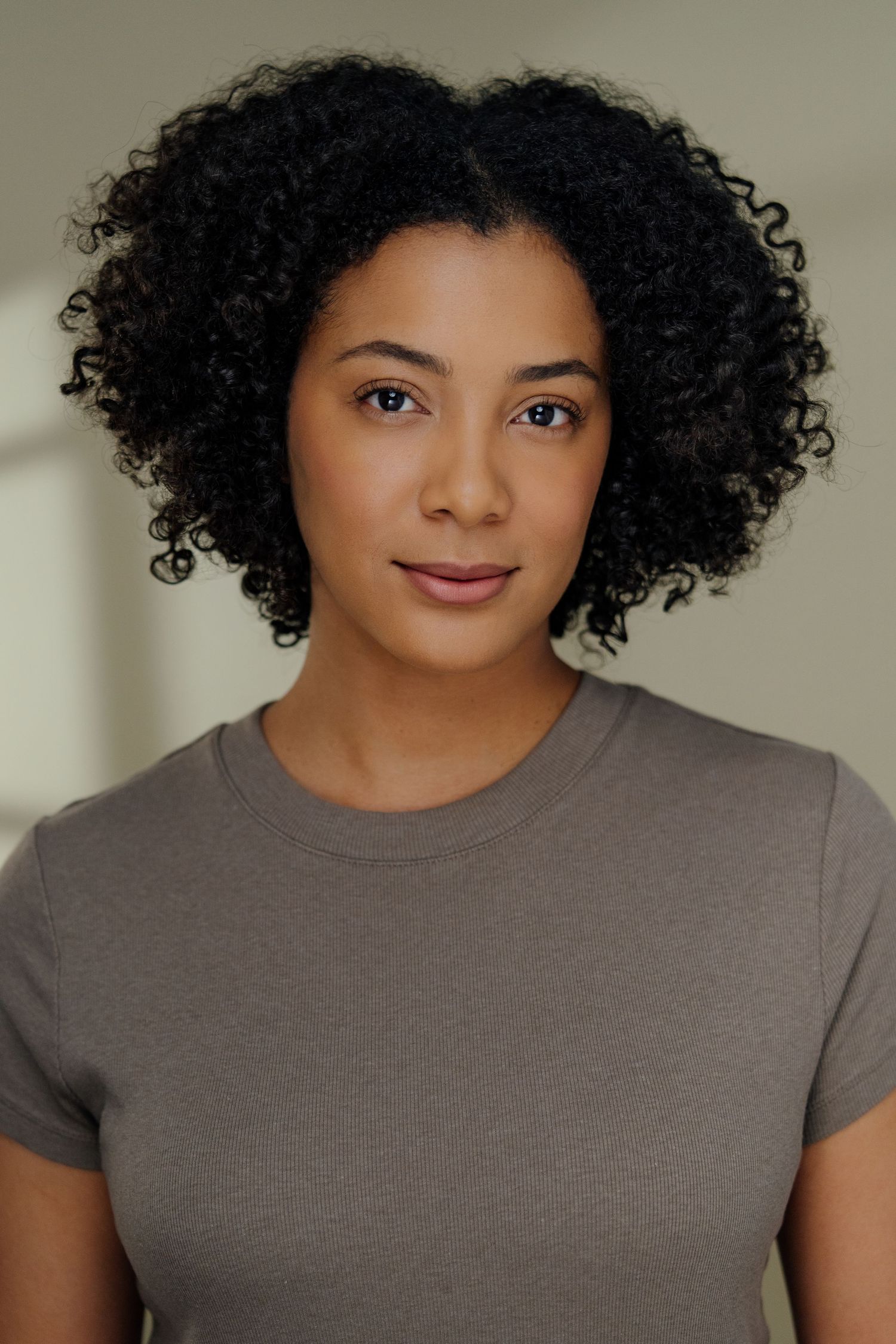 Woman with natural curly hair poses in gray t-shirt for professional portrait.