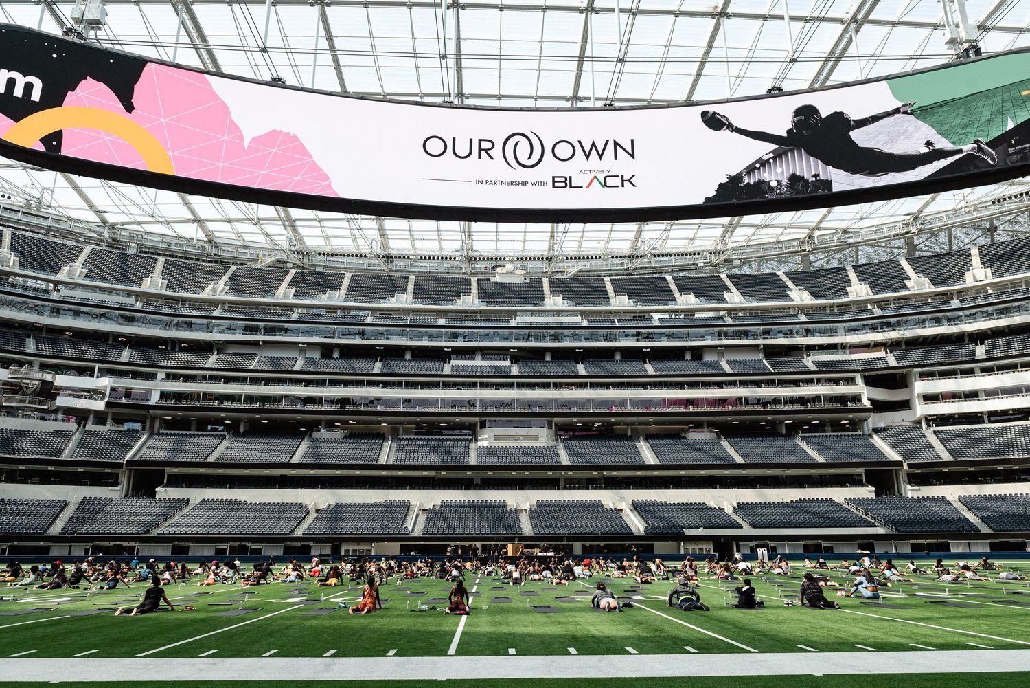 Wide angle view of a modern indoor sports arena with digital displays and green turf field.