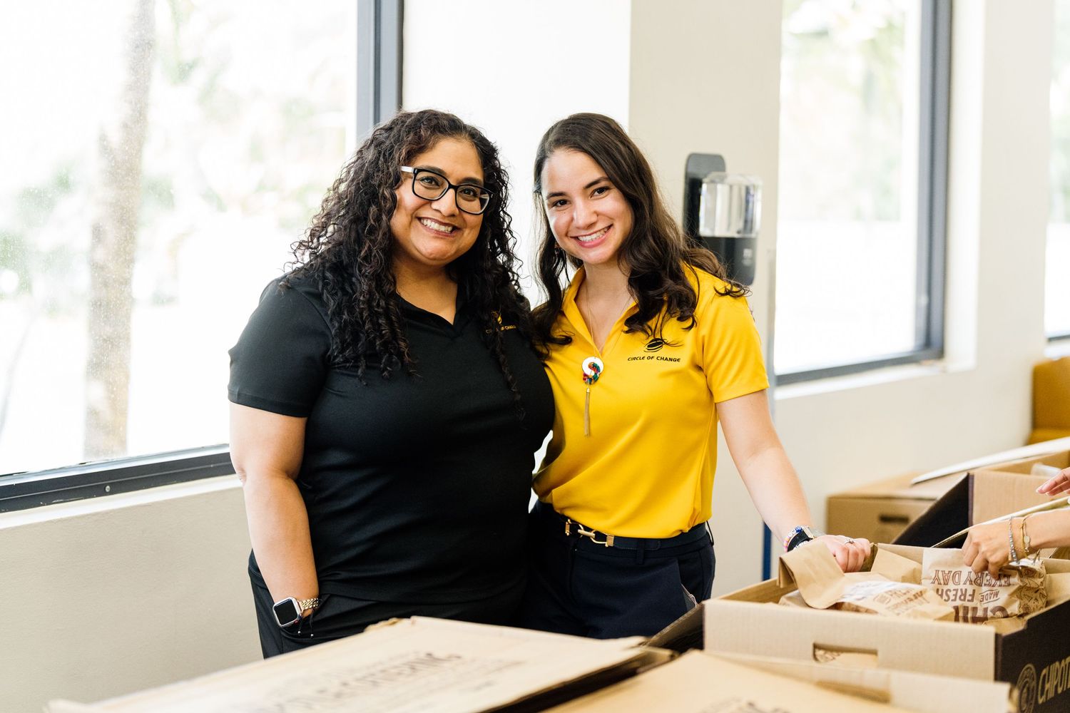 Two smiling women posing together at a desk inside a bright university building.