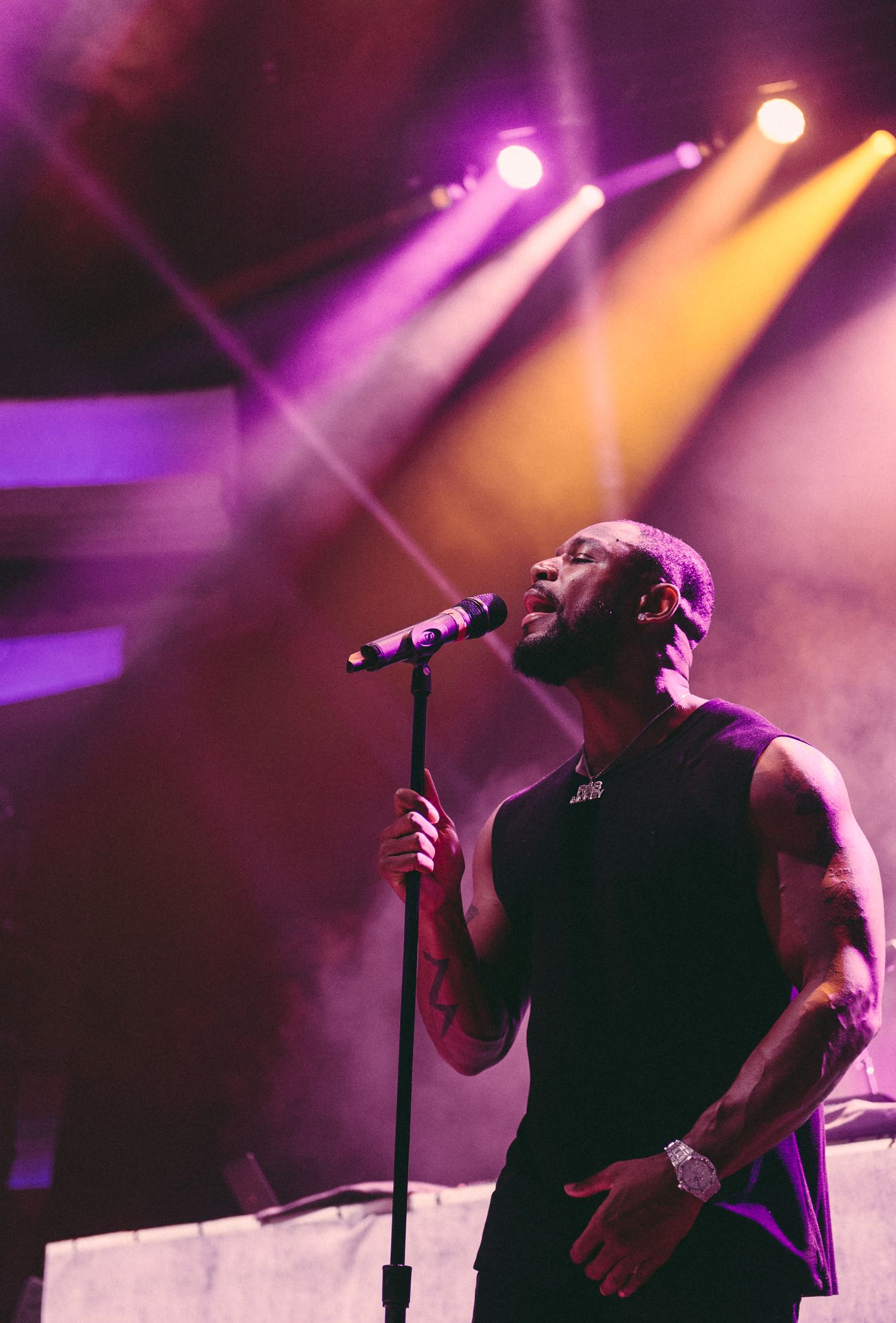 Concert performer on stage with vibrant purple and orange lighting effects.